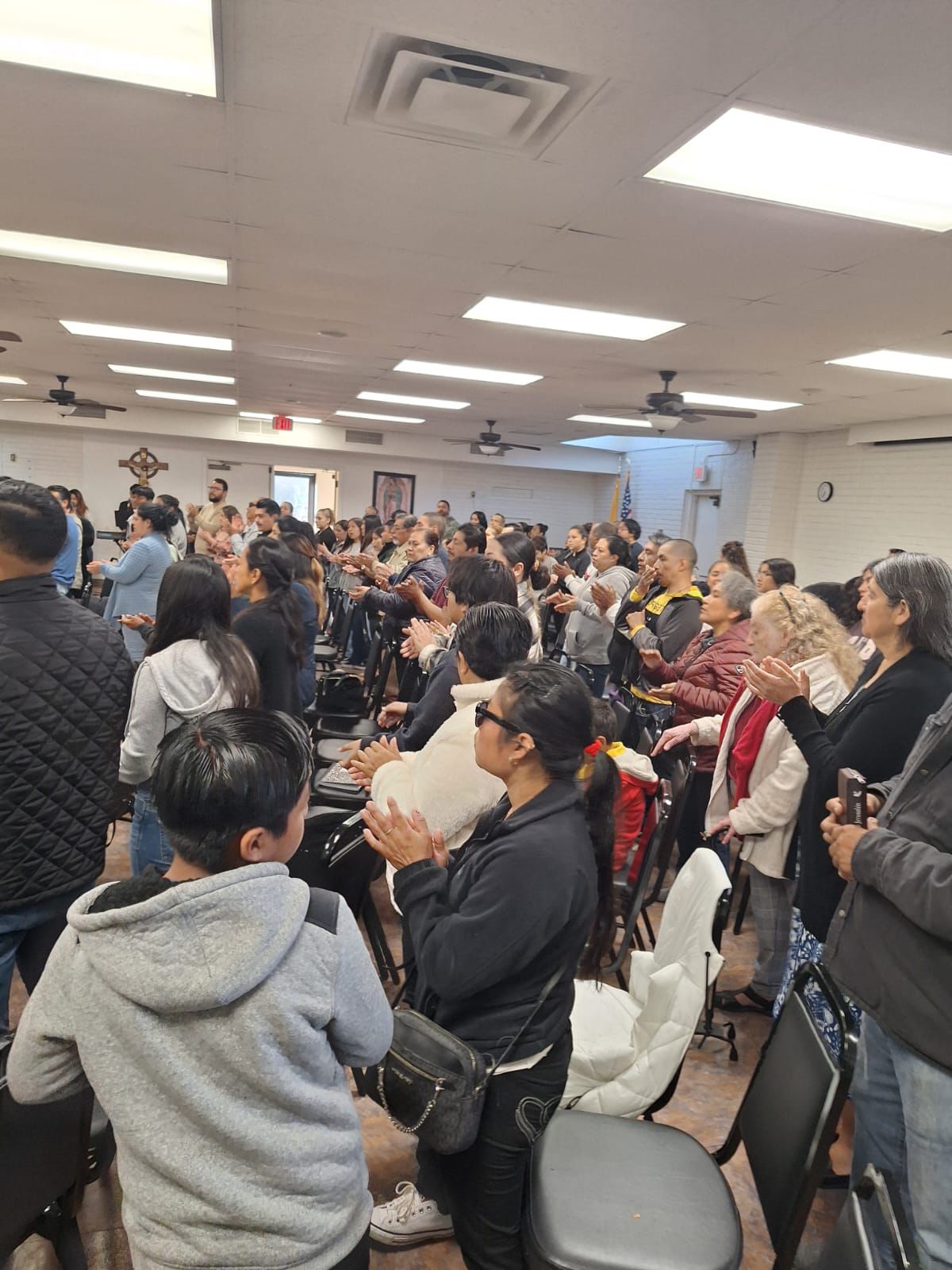 Crowded meeting room with many people standing and applauding under bright ceiling lights