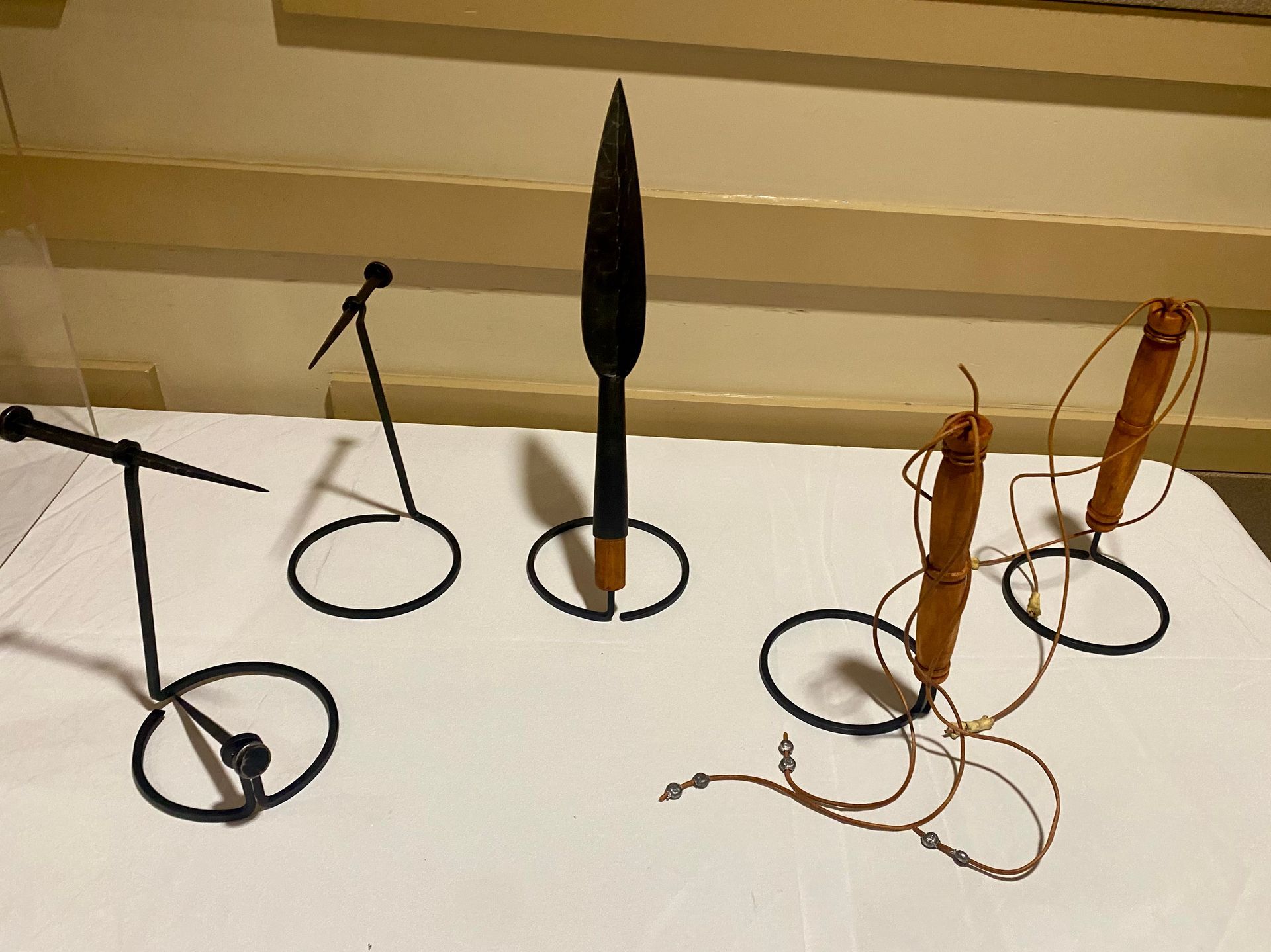 Display of assorted sculptures on a white table, including black wire figures and a tall dark central piece.