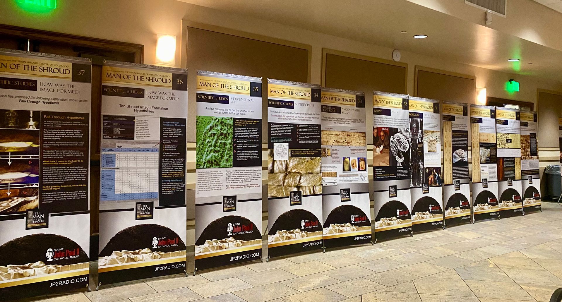 Row of promotional display boards with posters along a wall in a brightly lit indoor hall