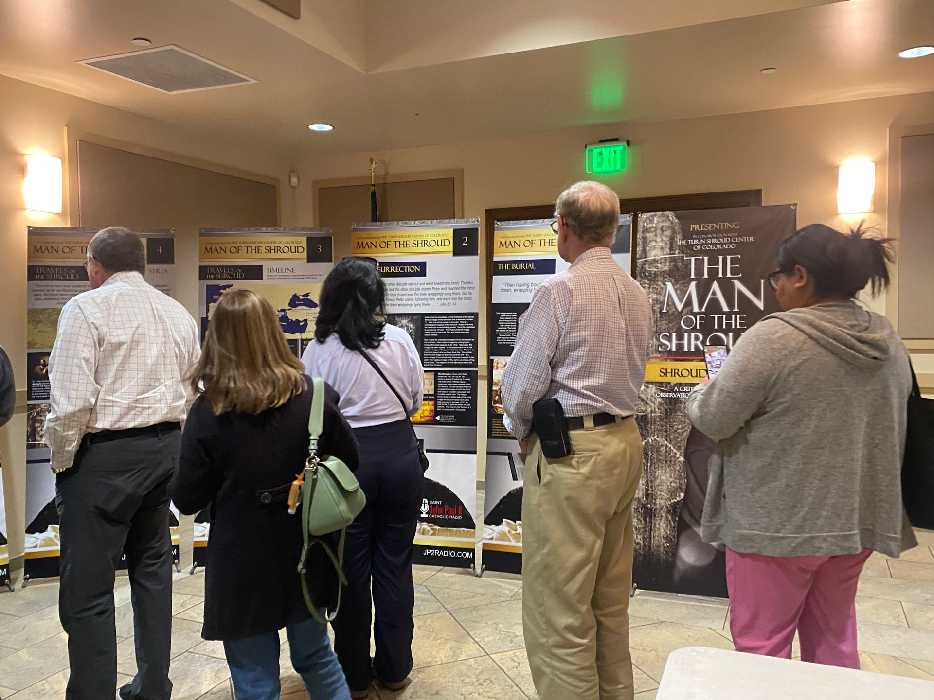 People viewing posters at an indoor event, with a large sign reading “THE MAN” in the background