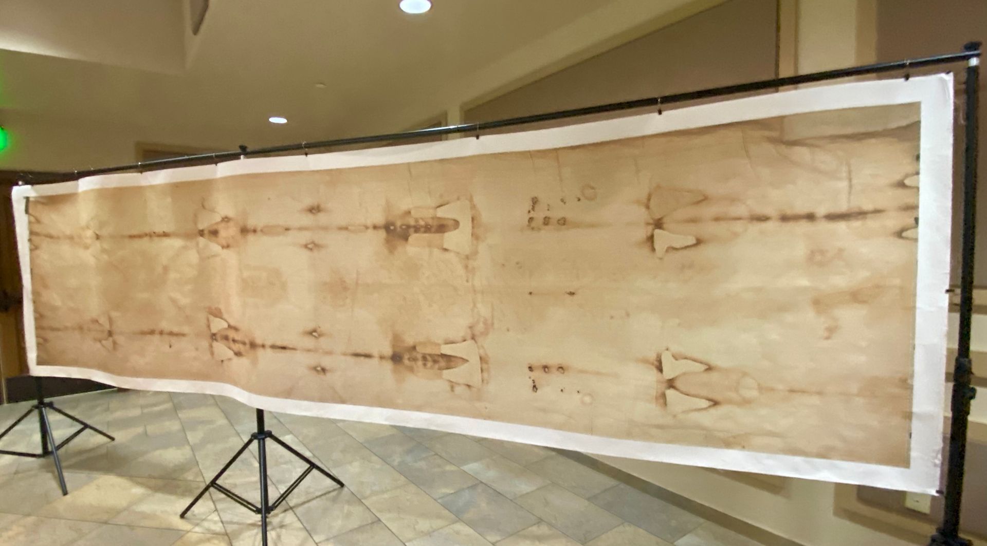 Large framed ancient linen cloth displayed in a museum, with faint reddish markings and support stands.