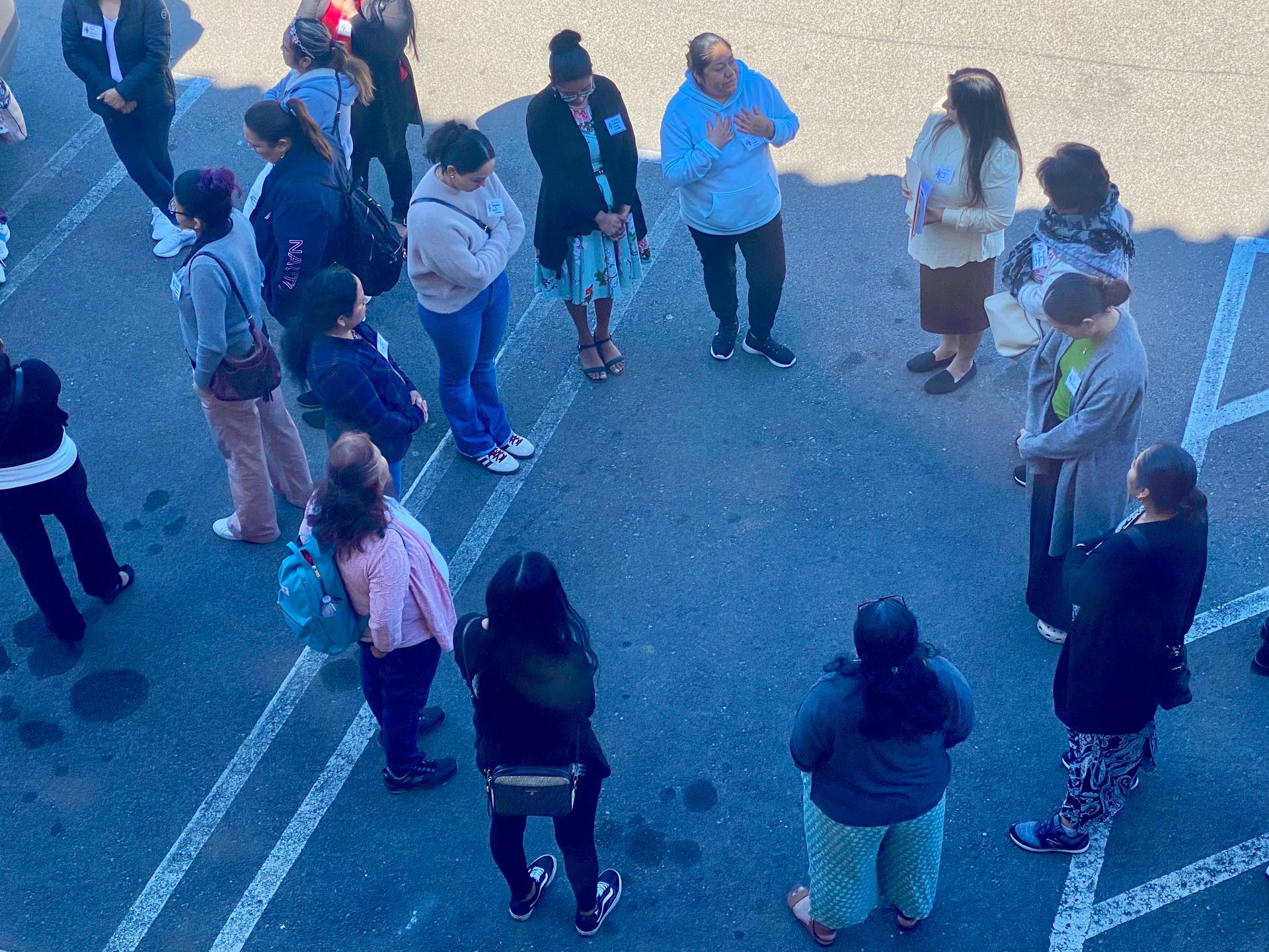 People standing in a loose circle on pavement, seen from above