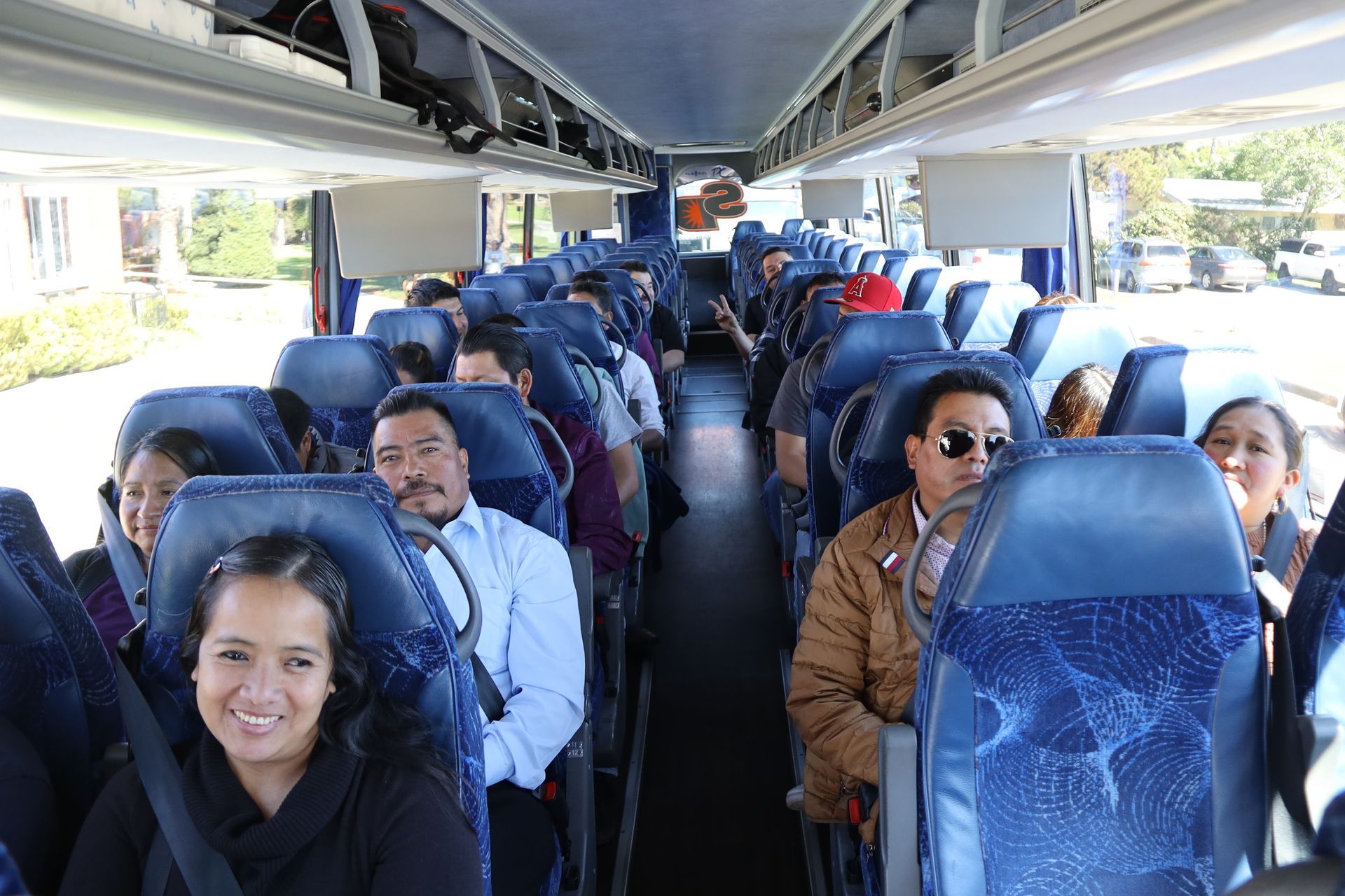 Passengers seated on a bus, with people looking toward the camera and daylight outside the windows