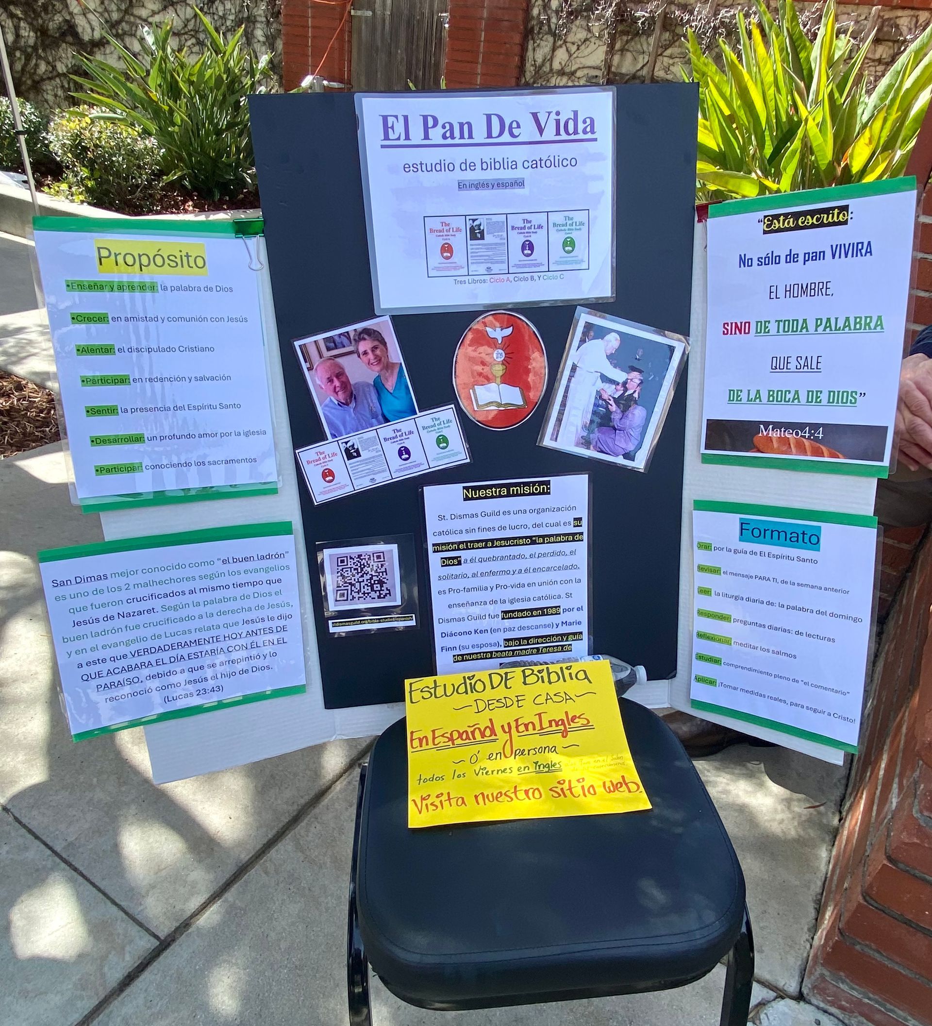 A black chair before a display board with colorful handwritten posters and photos outdoors.