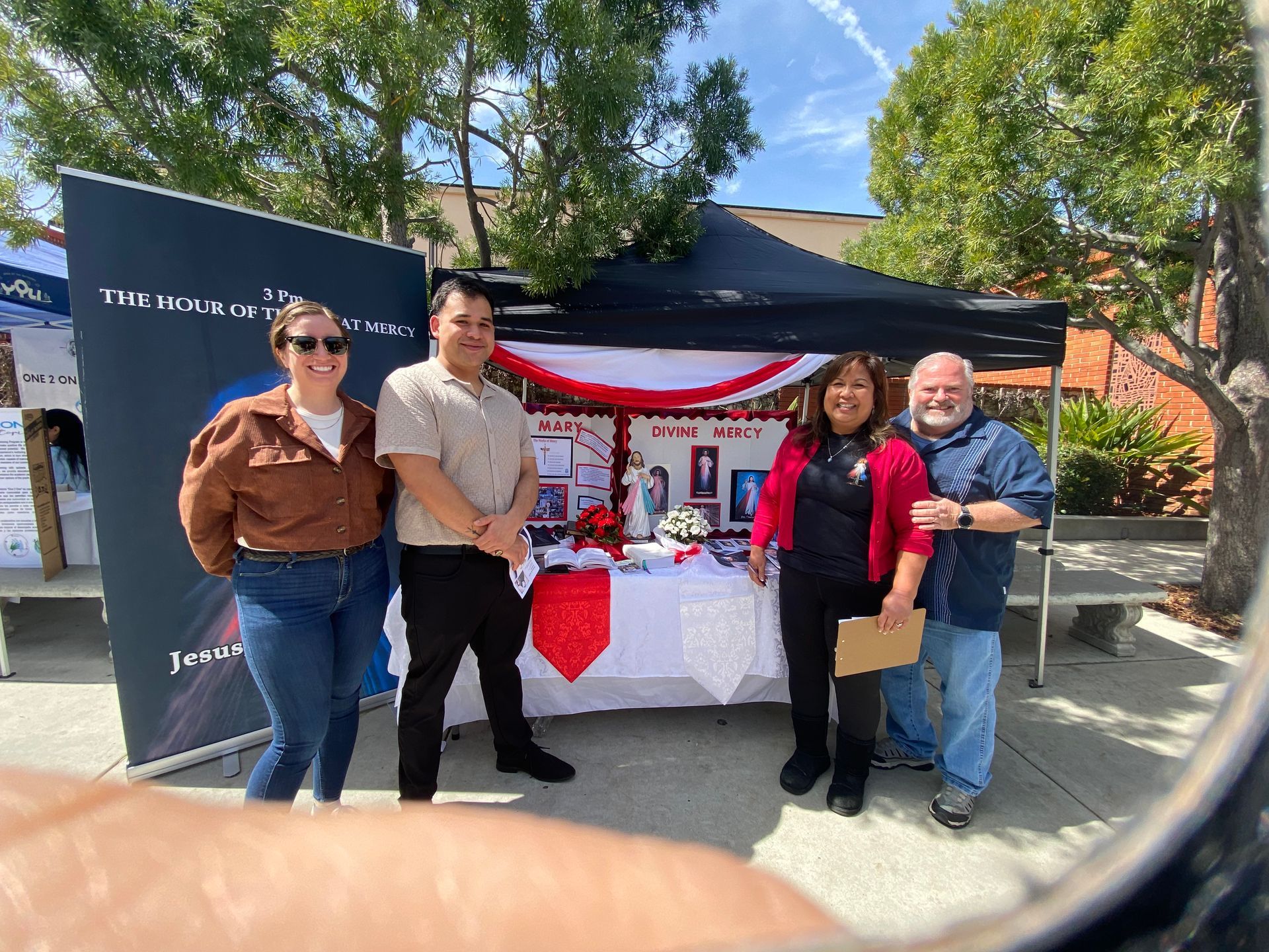 Four people stand at a decorated outdoor booth with a black canopy and red-and-white table display.