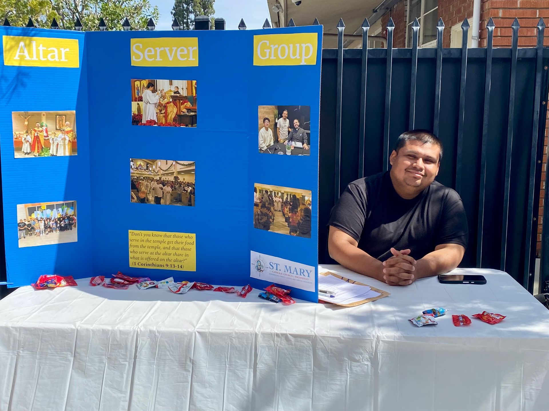Person at a blue event display booth with photos and signs, seated behind a white table.