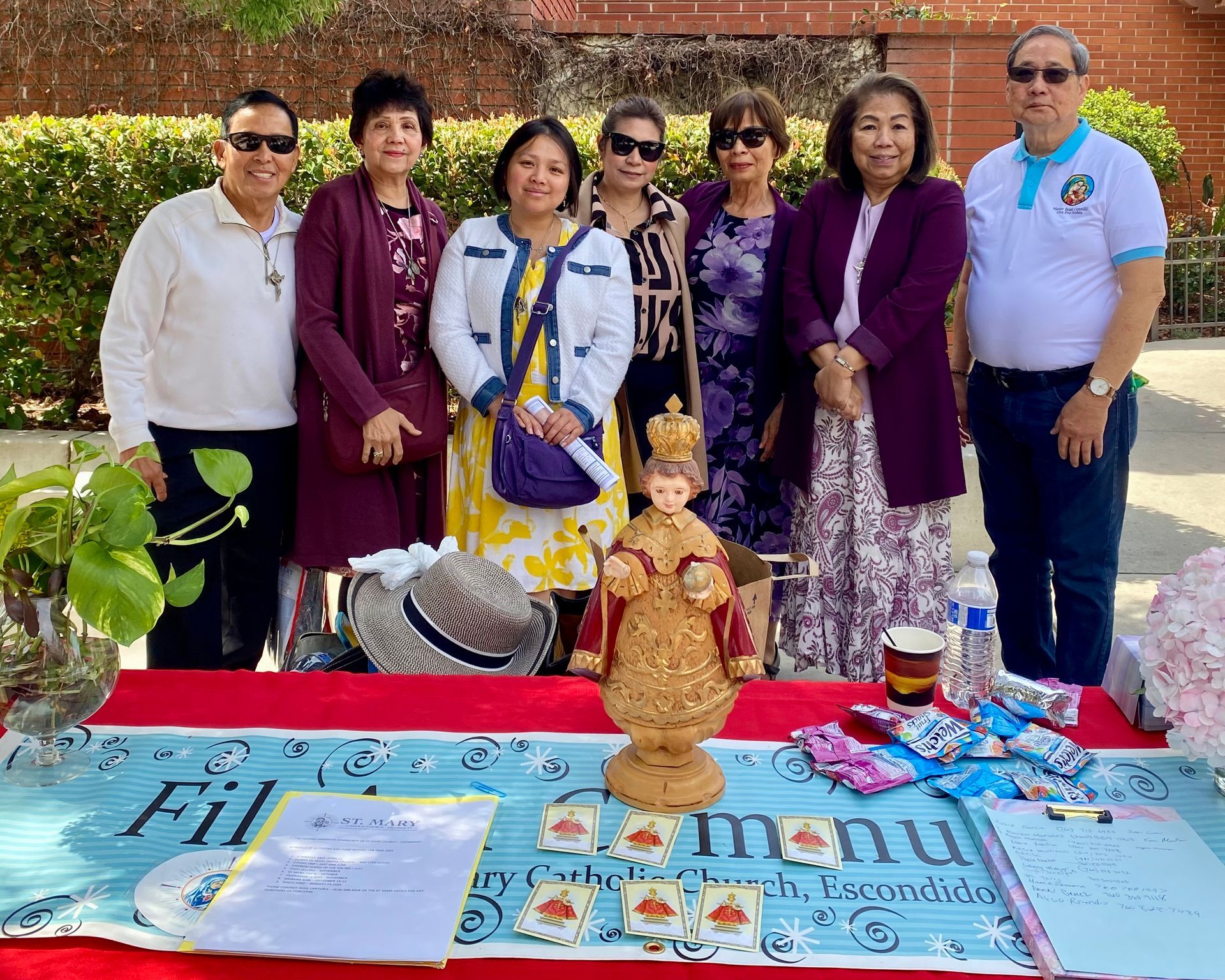 Six people posing outdoors behind a colorful table display with a decorative figurine and printed materials.