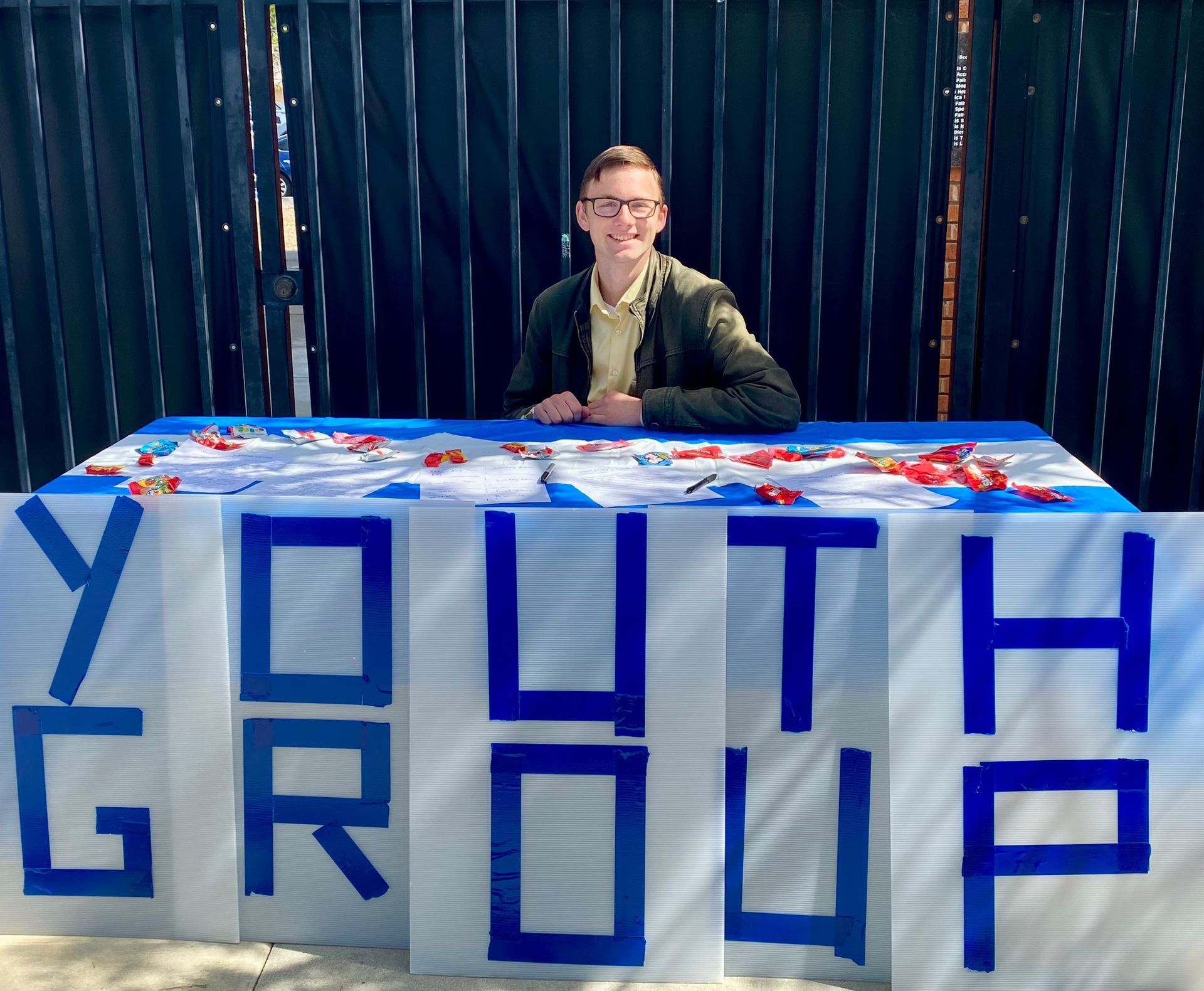 Person behind a table with a large blue “YOUTH GROUP” sign and red-white-blue decorations.