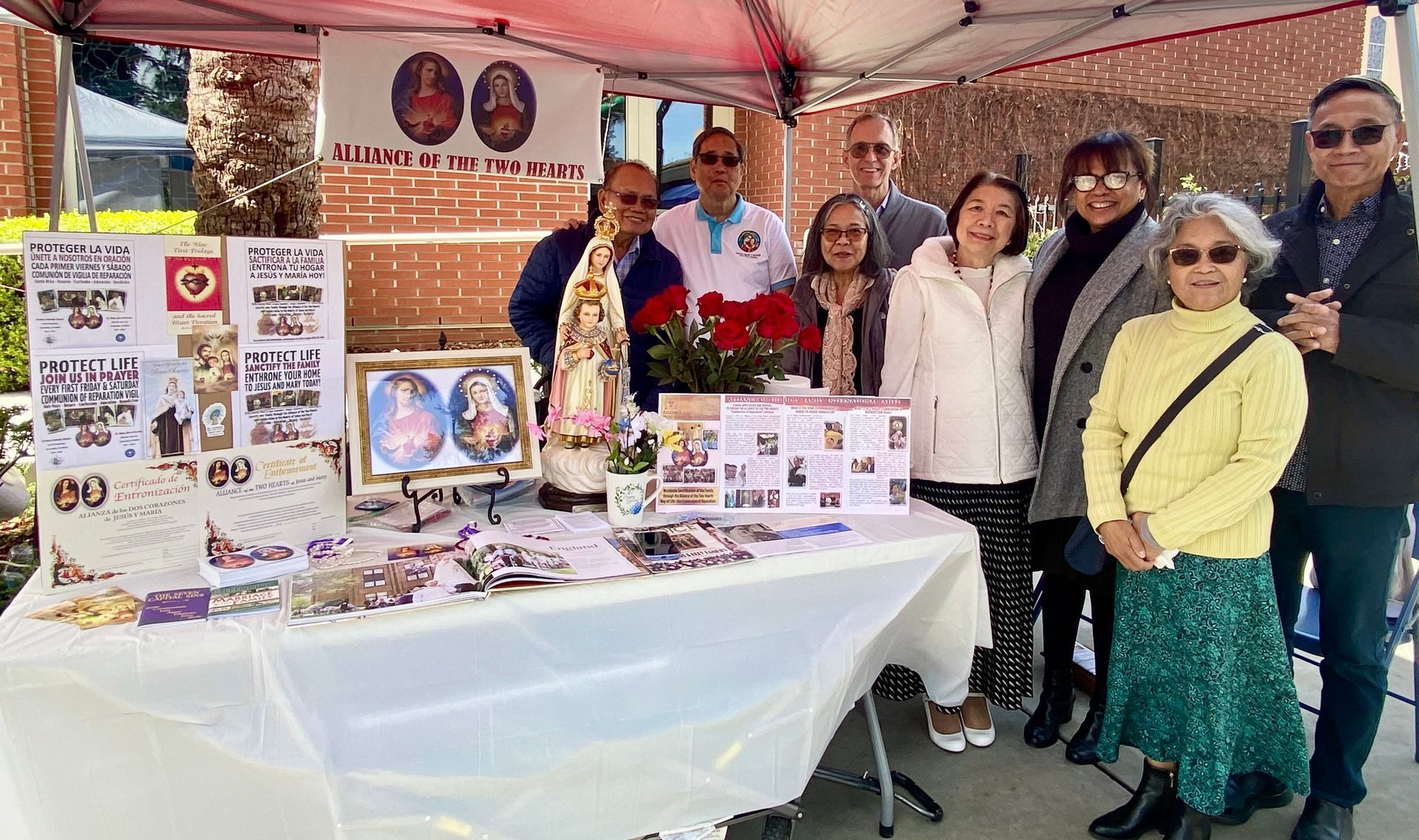 Group at a table under a tent, displaying handmade items and photos at a community booth