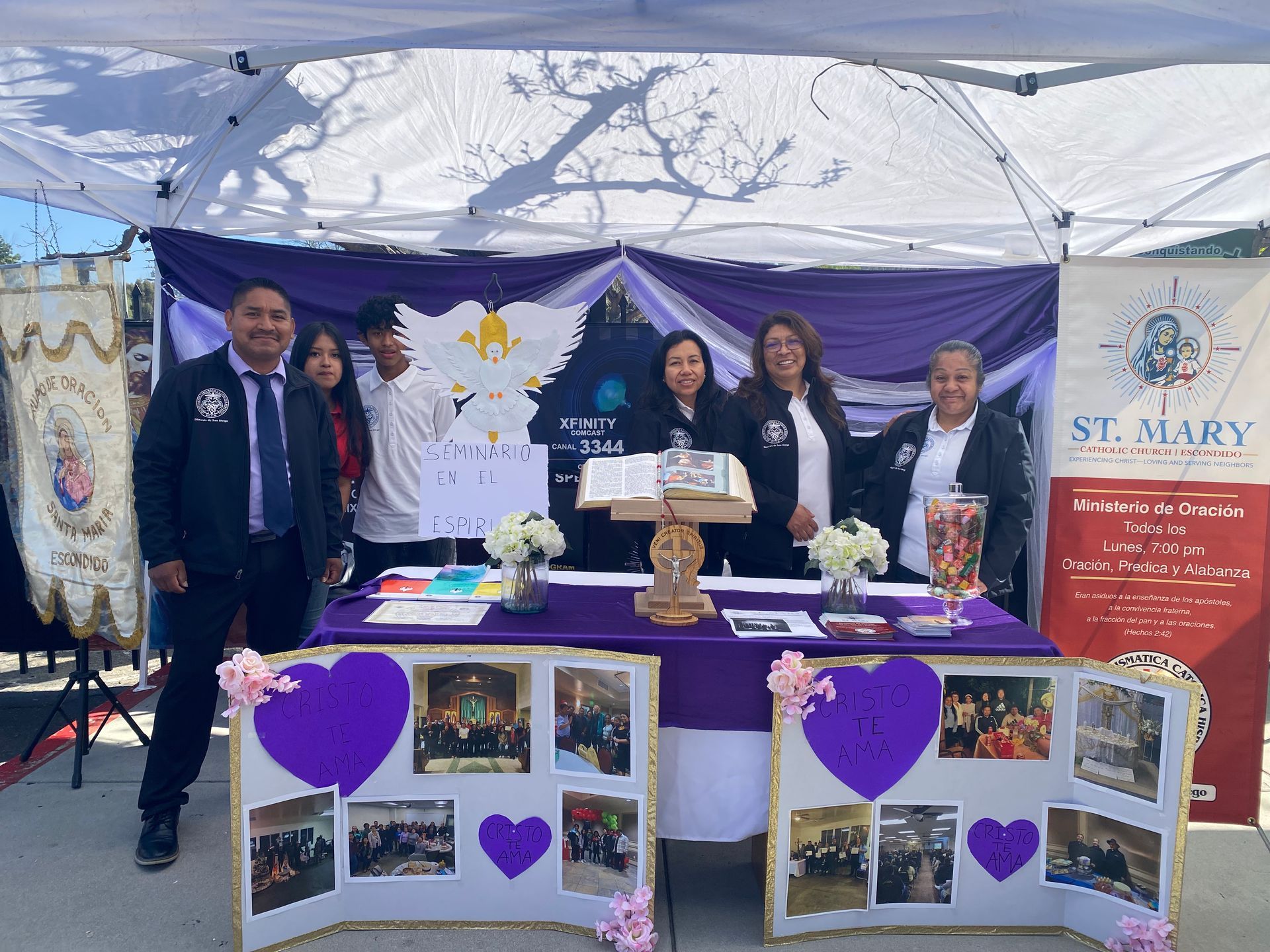 People at a St. Mary booth with purple heart decorations and display boards under a white tent.