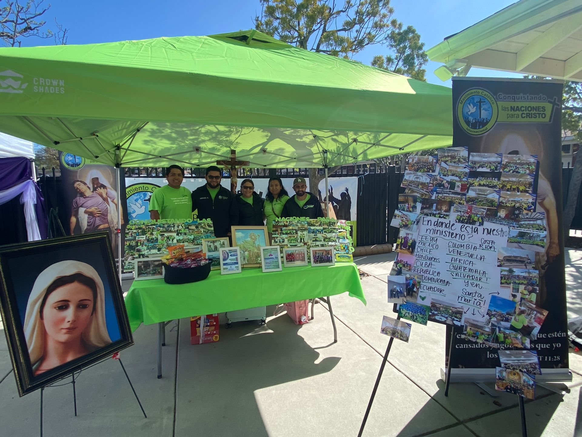 Green outdoor booth with people, posters, and a display board at a community event