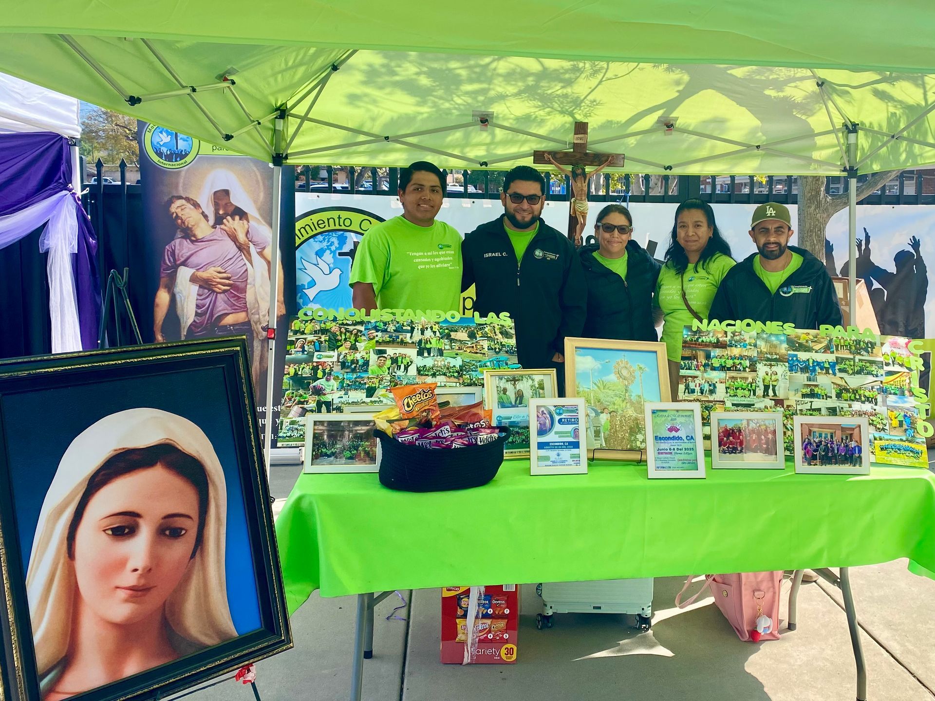 Vendor booth under green canopy with framed art and photos displayed on a neon-green table