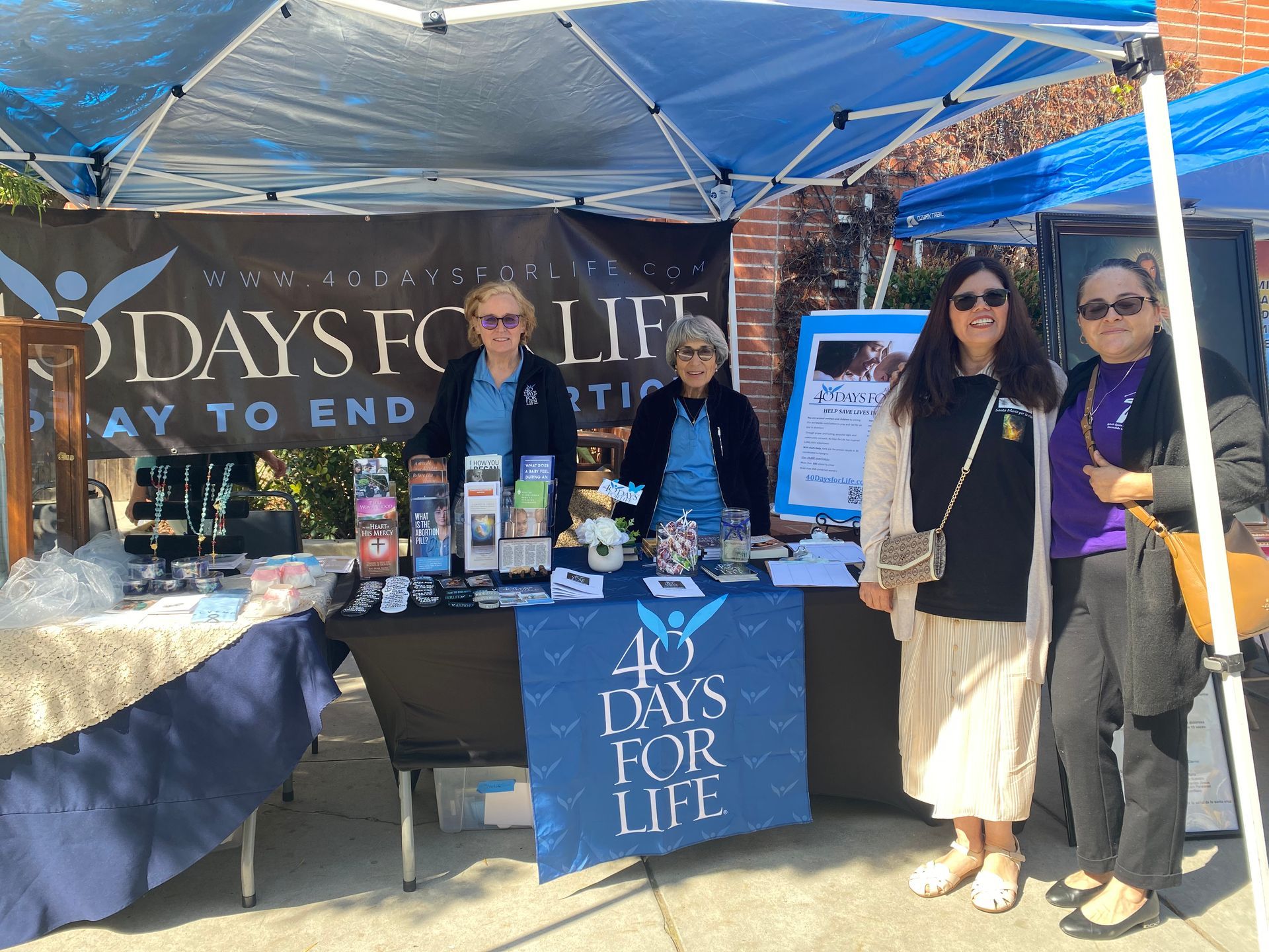 Days for Life outreach booth under blue canopy with volunteers and display table outside storefront