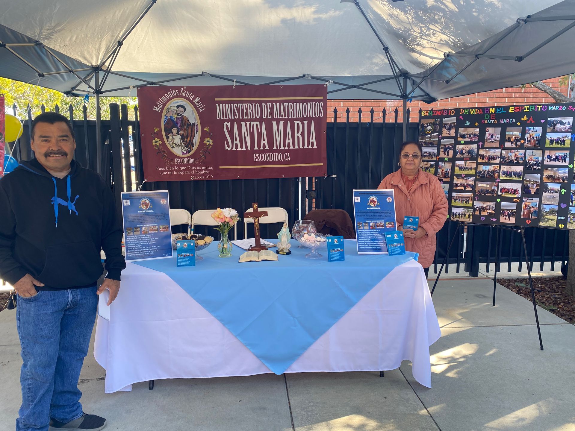 Booth under a canopy with a banner, table display, and two people standing beside it.