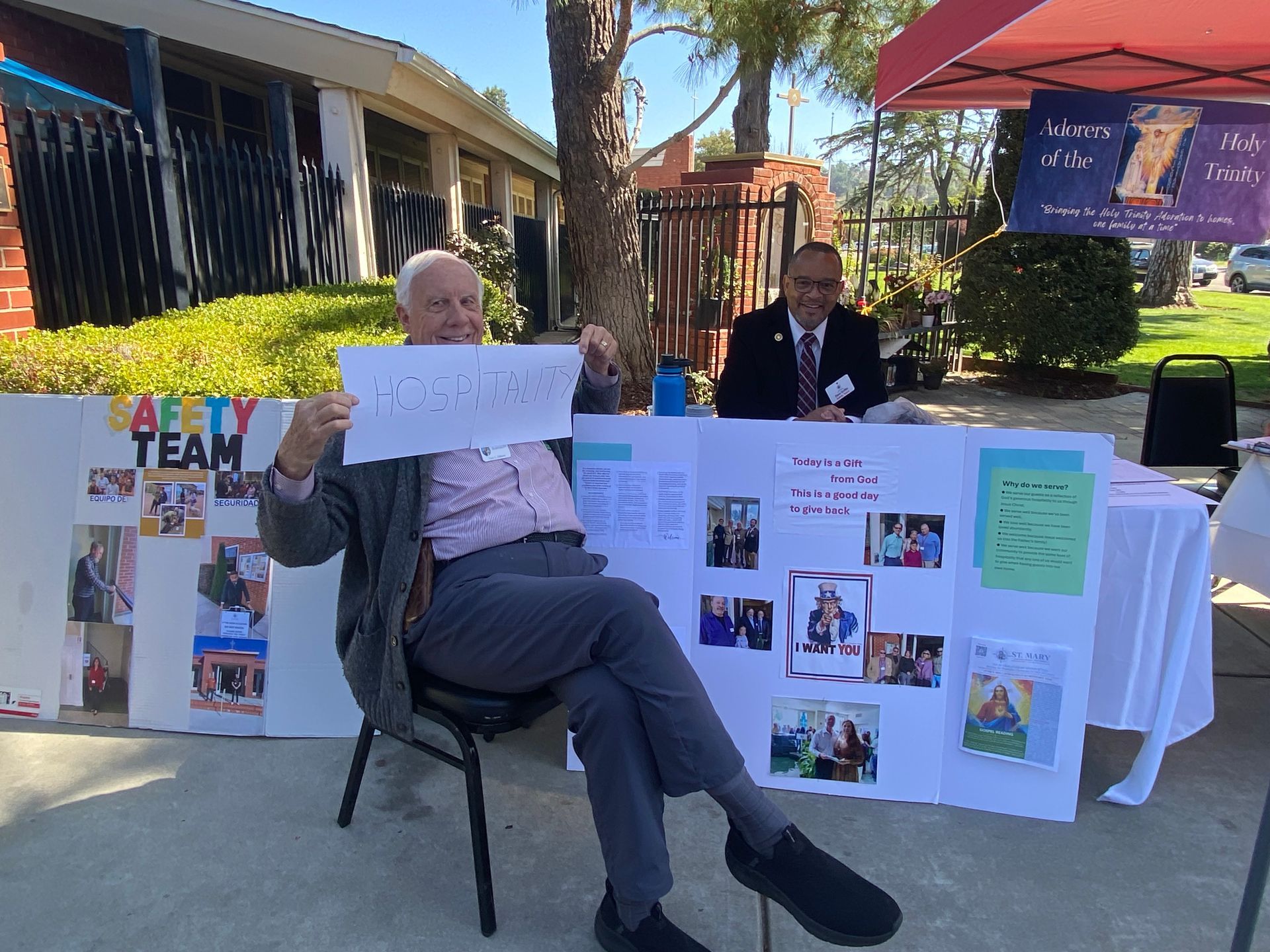 Outdoor booth with poster boards and a seated person in a dark suit behind a white tablecloth at a campus event