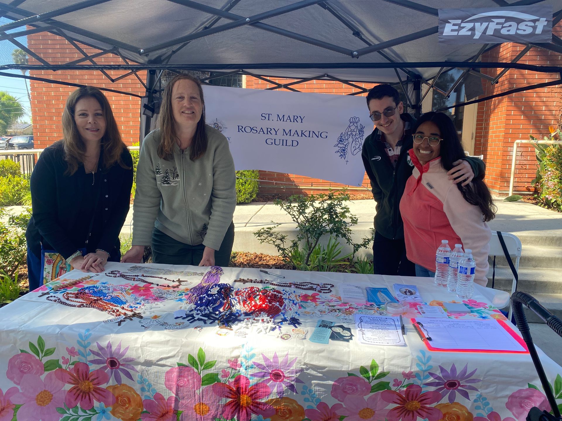 Four people stand behind a decorated table at an outdoor EzyFast booth under a canopy.