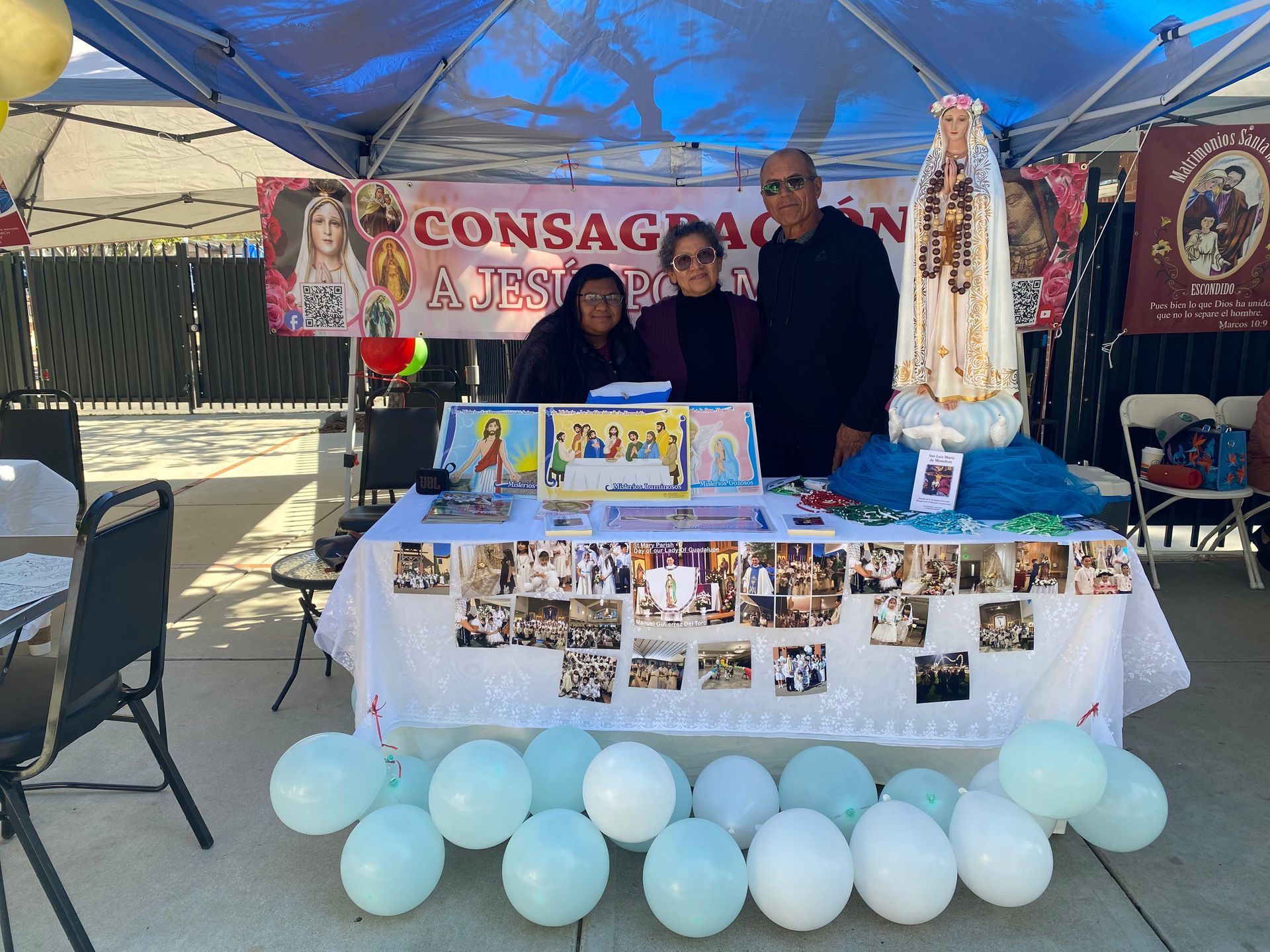 Outdoor memorial booth with banners, photos, candles, and blue balloons under a canopy