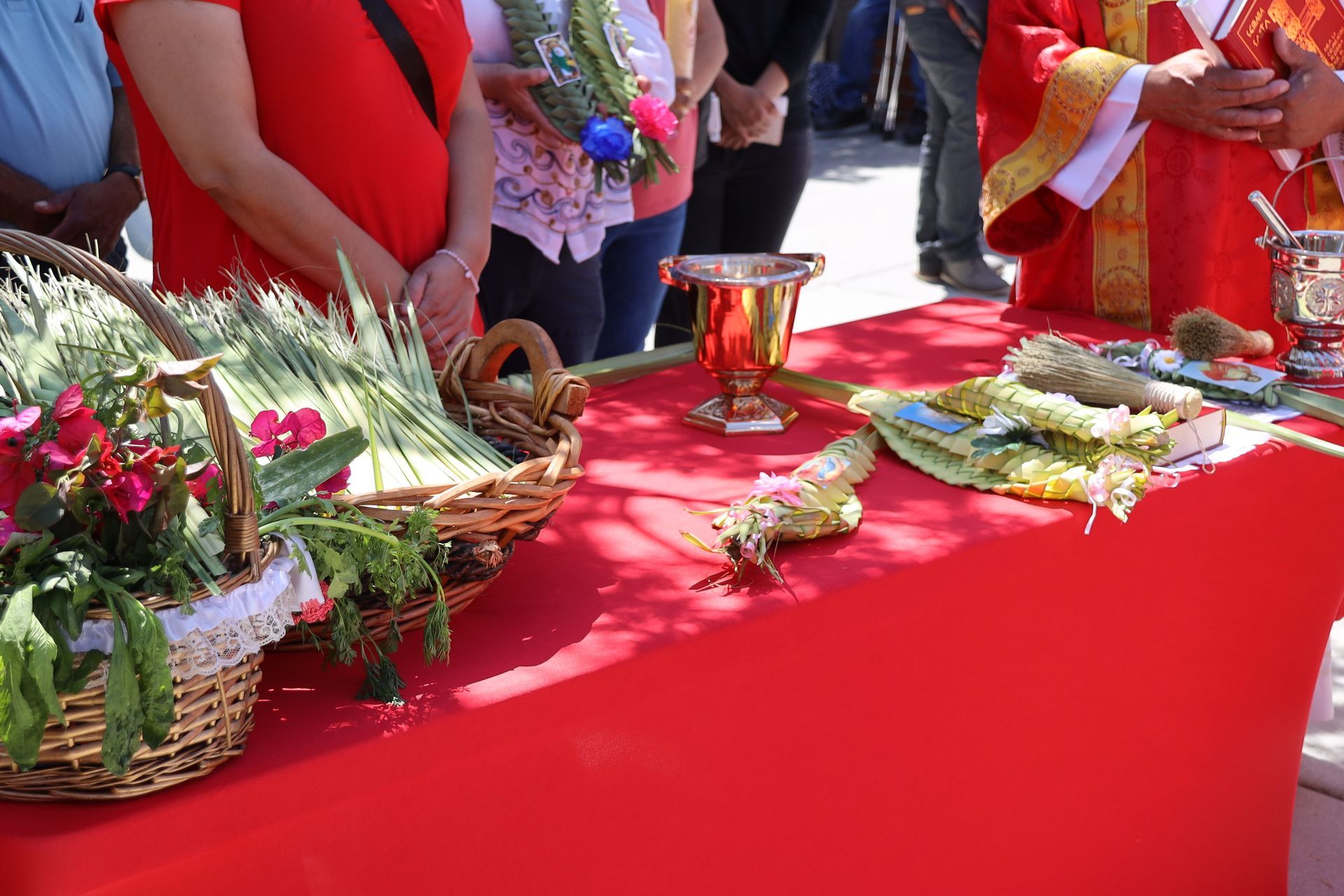 Red table with baskets of flowers and trays of offerings at a festive outdoor ceremony