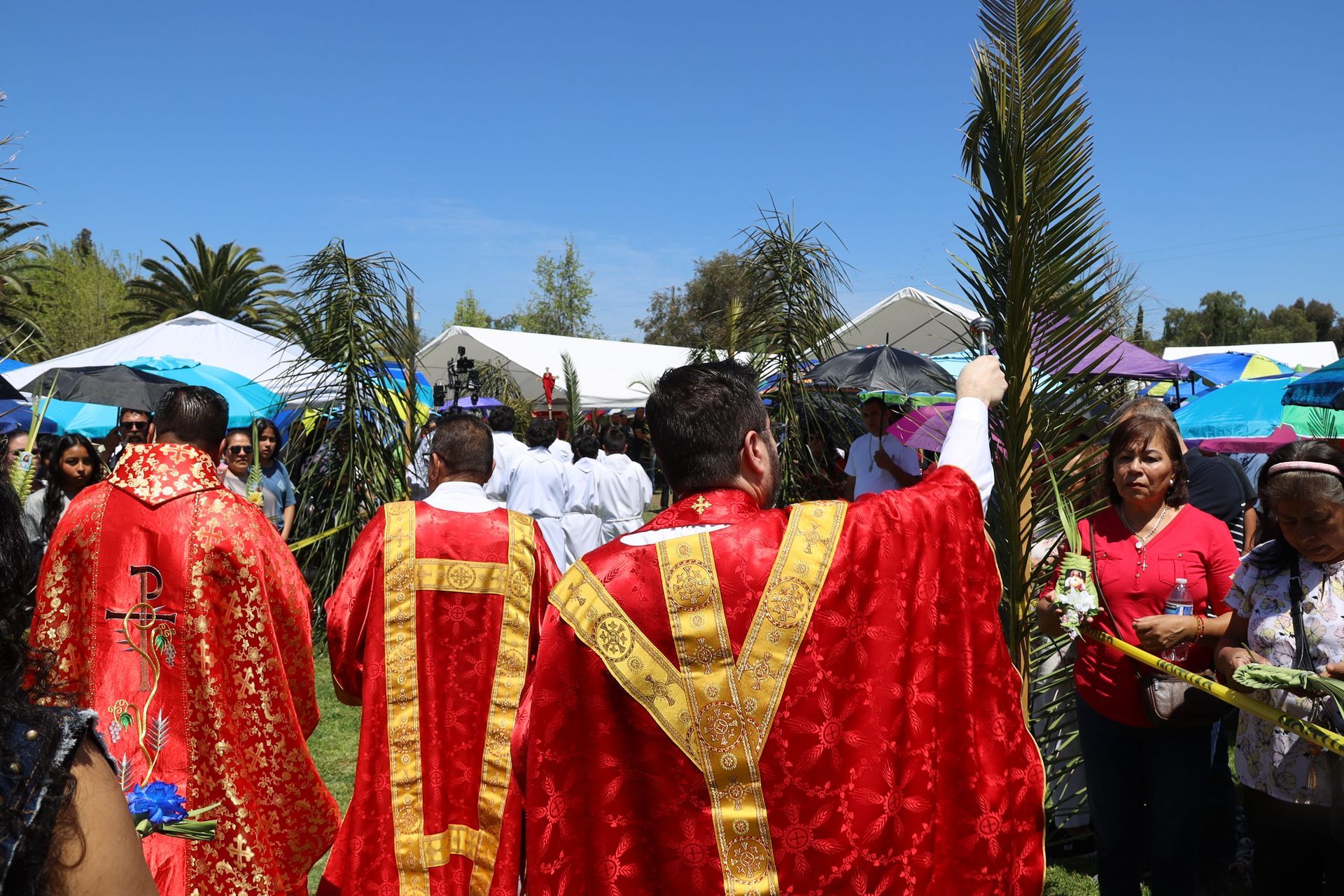 People in red and gold robes celebrating outdoors under a bright blue sky