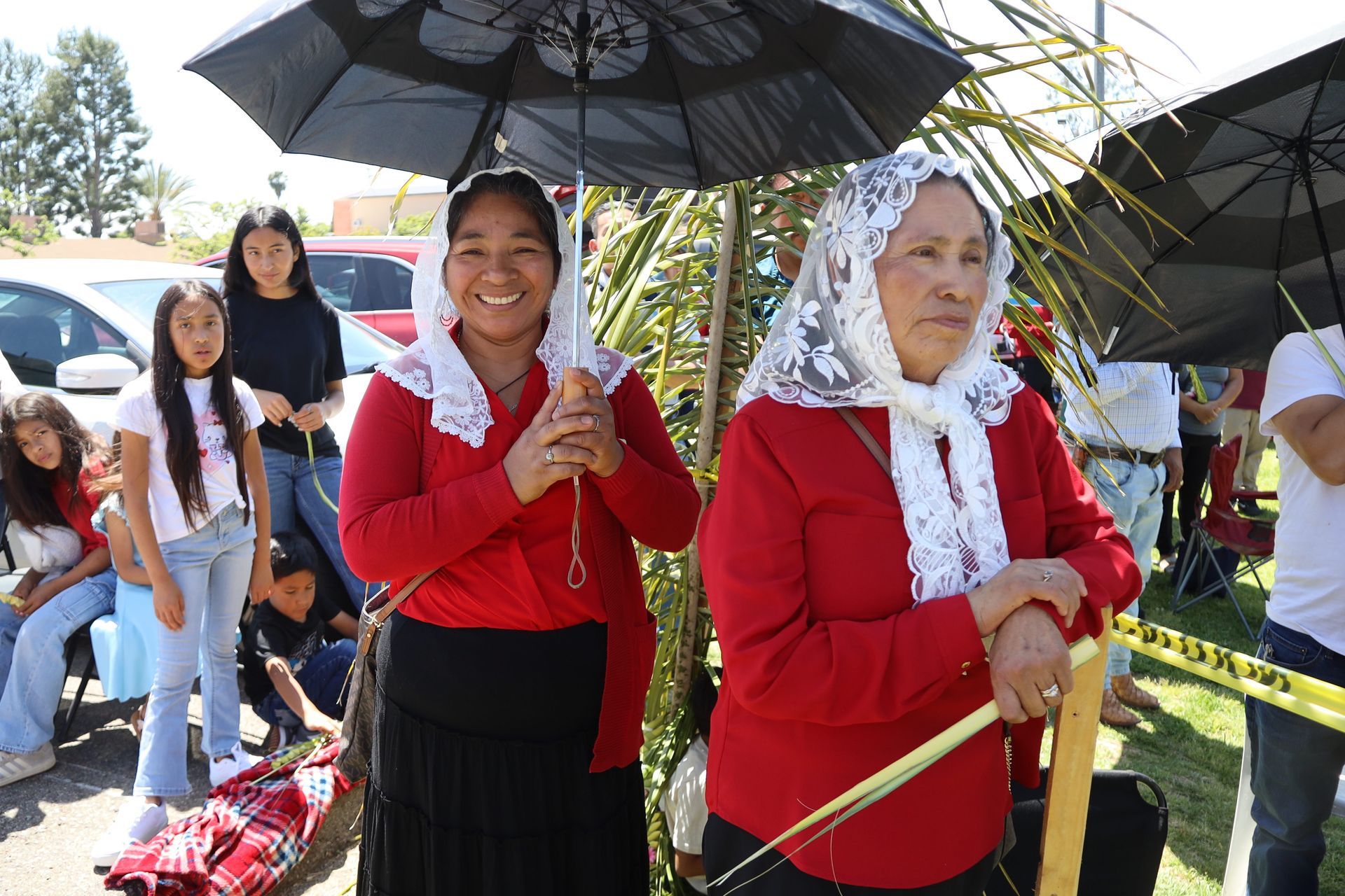 Two women in red outfits holding black umbrellas at an outdoor event