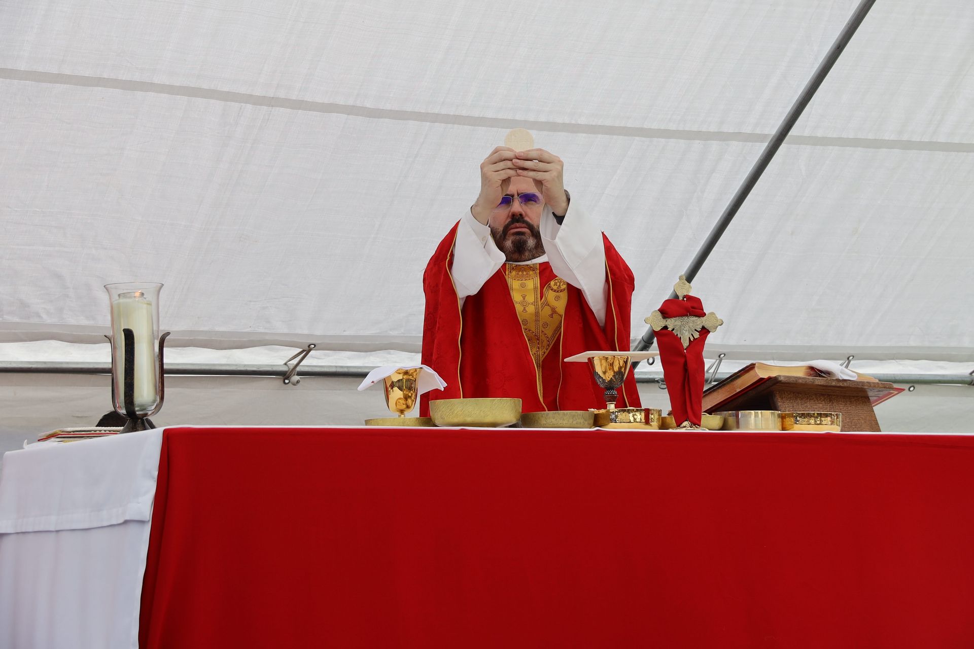 Clergy in red vestments standing behind an altar under a white tent