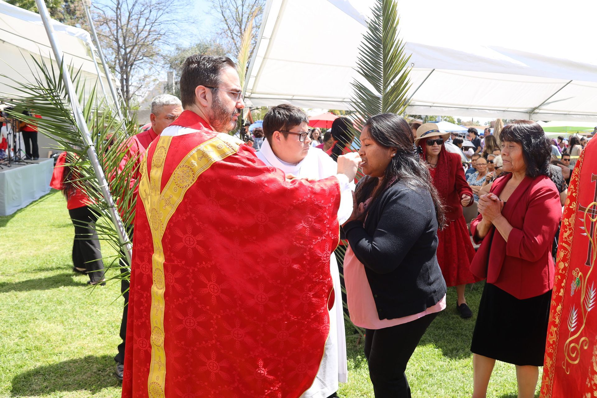 Outdoor ceremony with people in red robes greeting attendees under a white tent