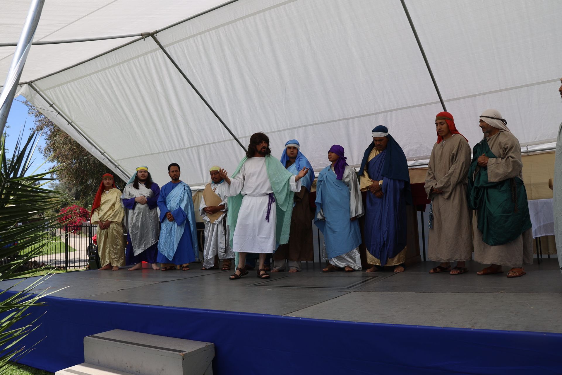 People standing on an outdoor stage under a white tent, wearing colorful robes and coats