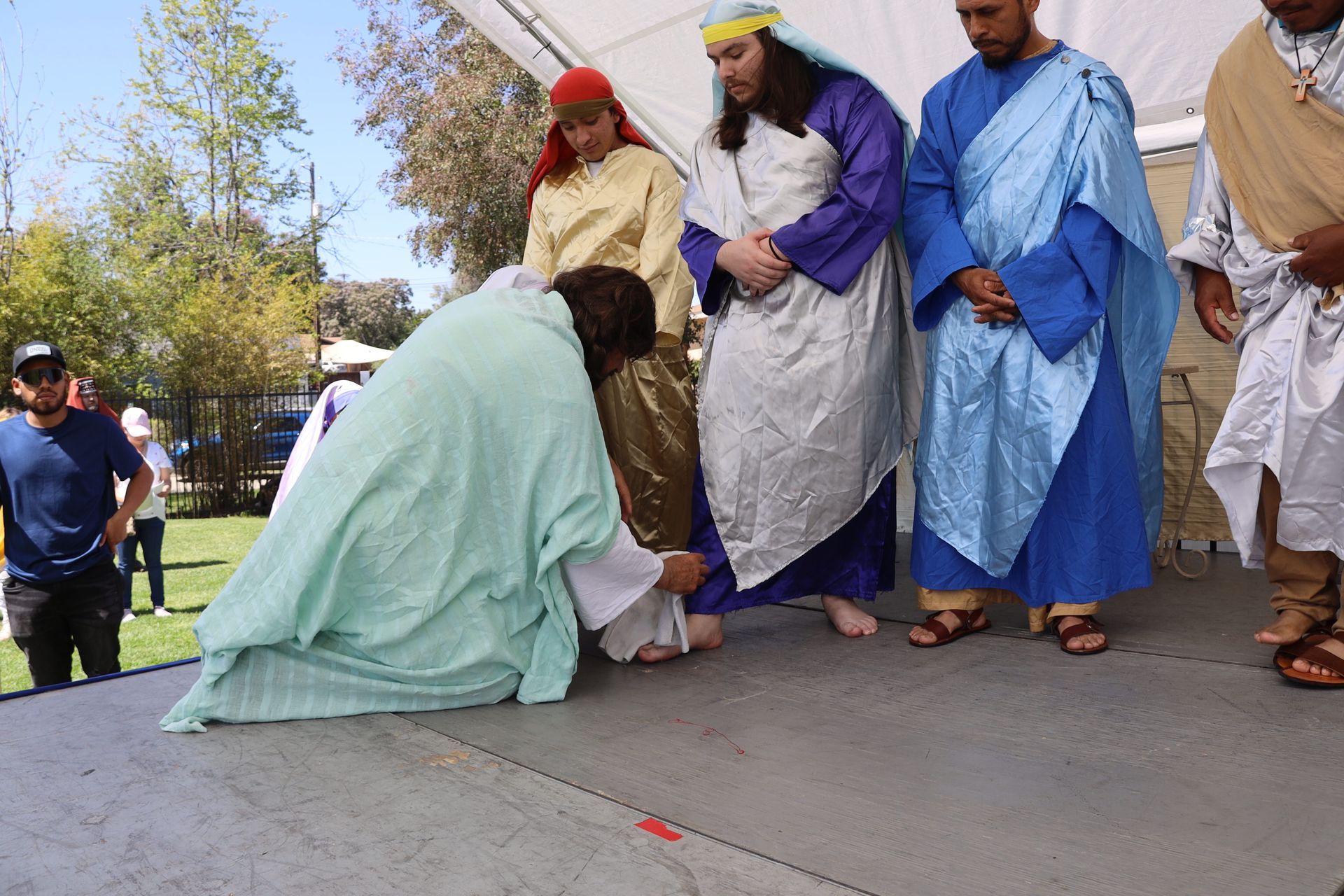 People in colorful robes stand around a kneeling person outdoors on a paved area.