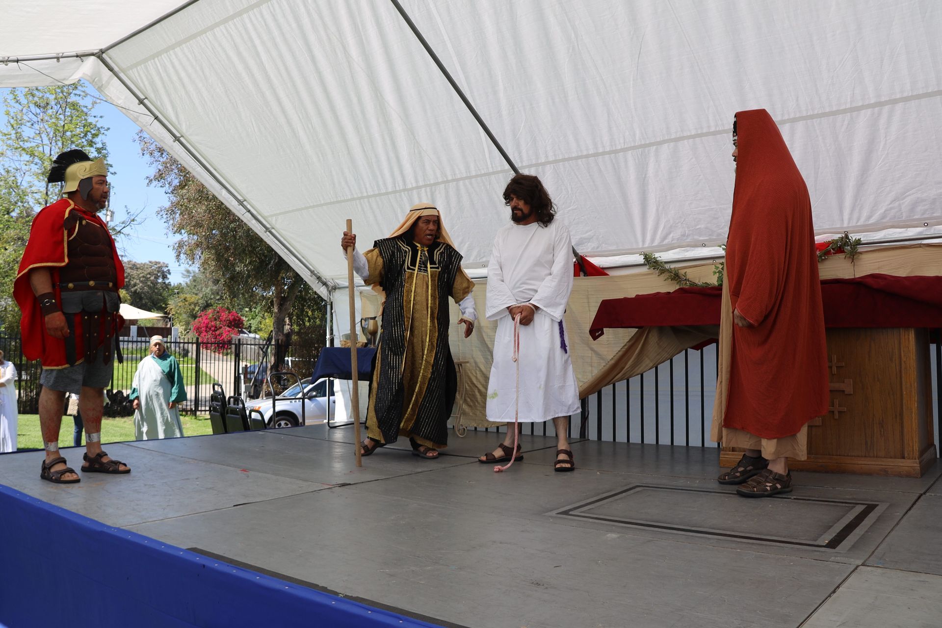 People in costumes standing on an outdoor stage under a white canopy