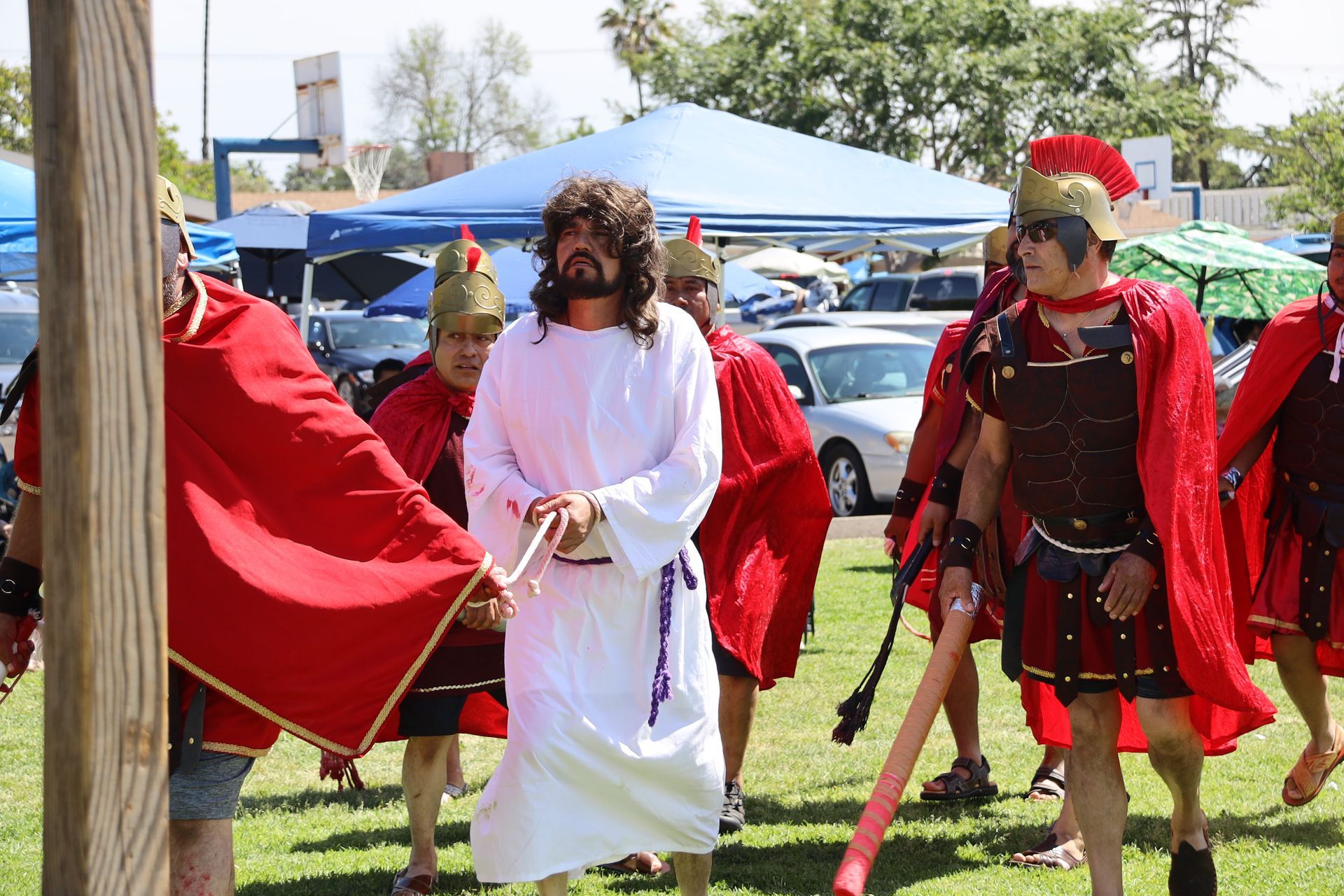 People in red and white costumes standing on grass outdoors, one holding a sword.