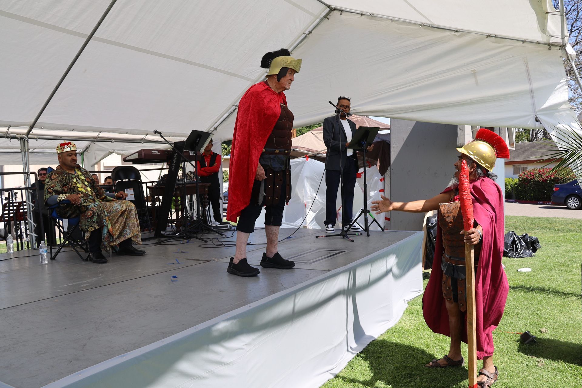 Costumed performers on a stage under a white tent during an outdoor event