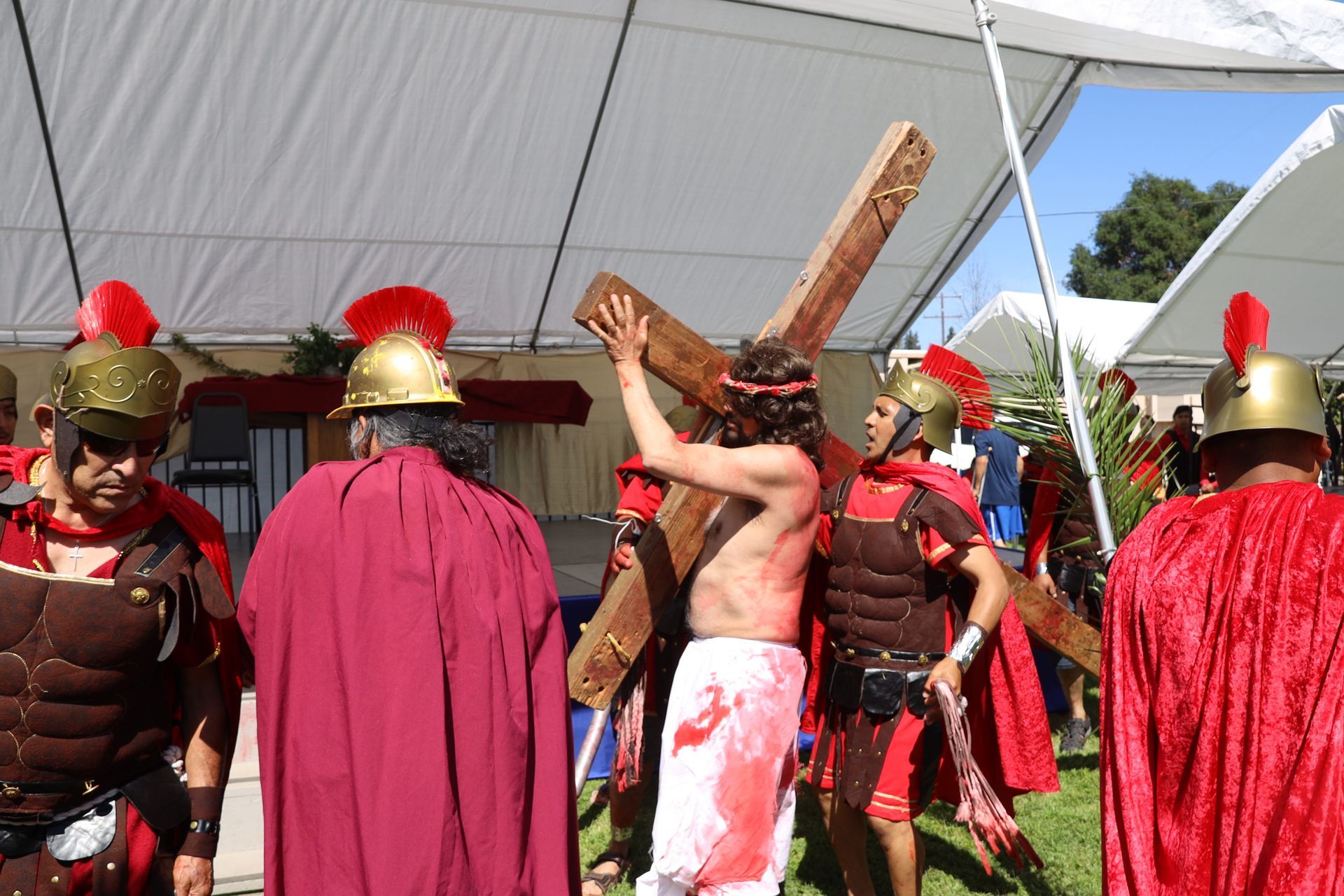 People in red costumes and Roman-style helmets performing outdoors under a white tent