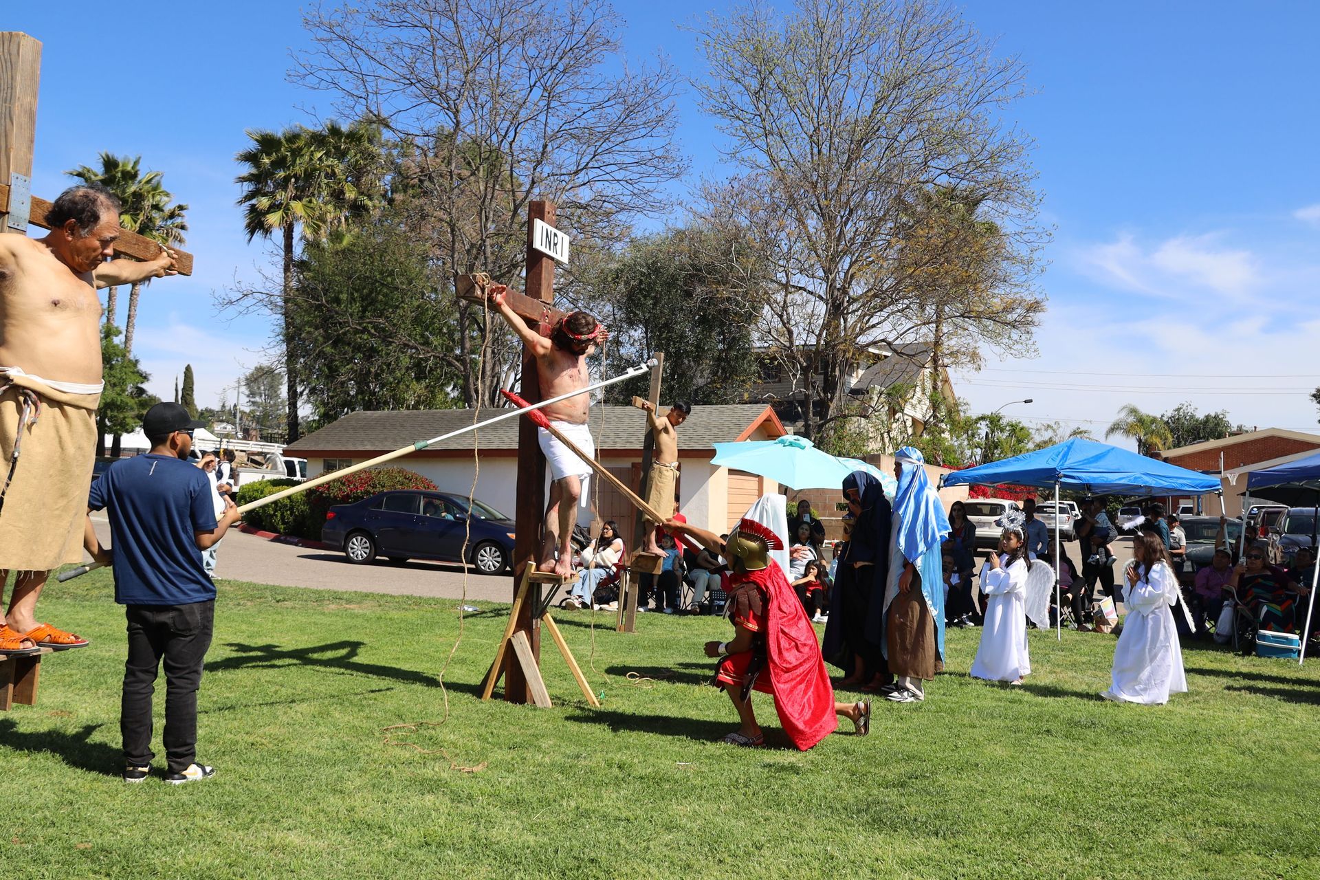 Outdoor cultural performance on a grassy field with performers in costumes and an audience under tents