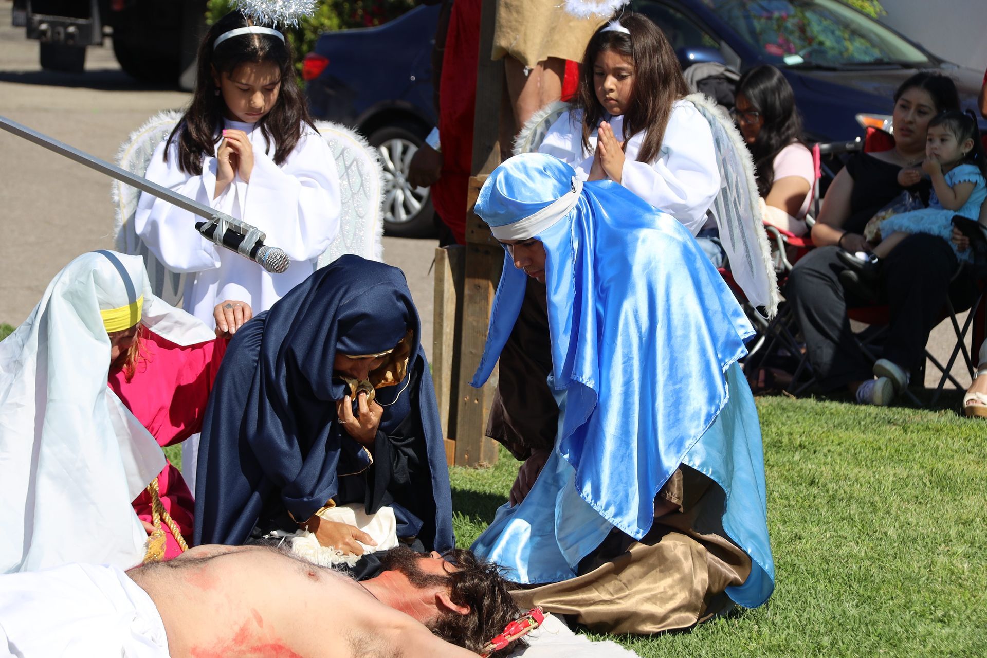 Children in costumes reenact a Nativity scene outdoors on grass.
