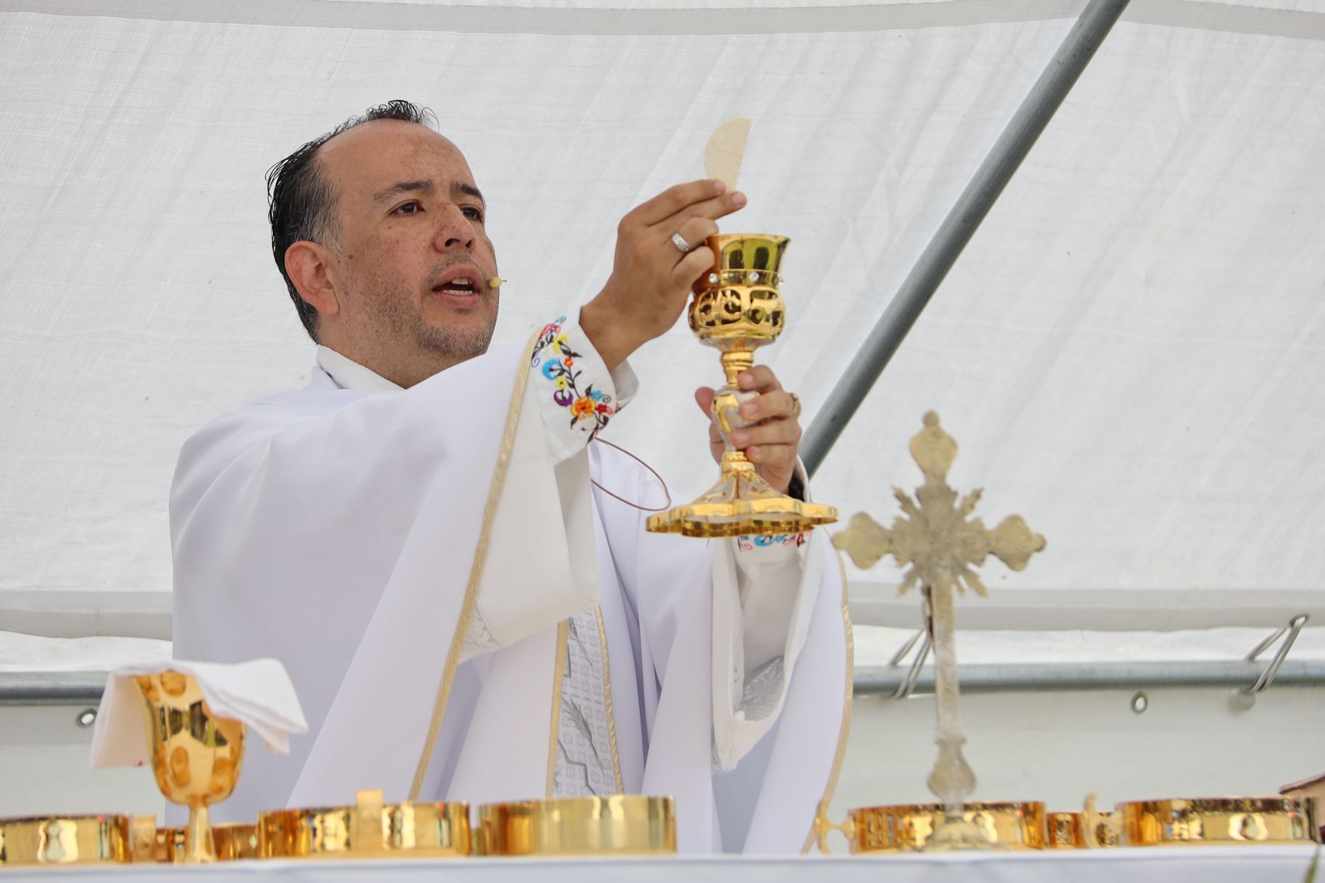Priest in white robe lifting a gold chalice during a church ceremony