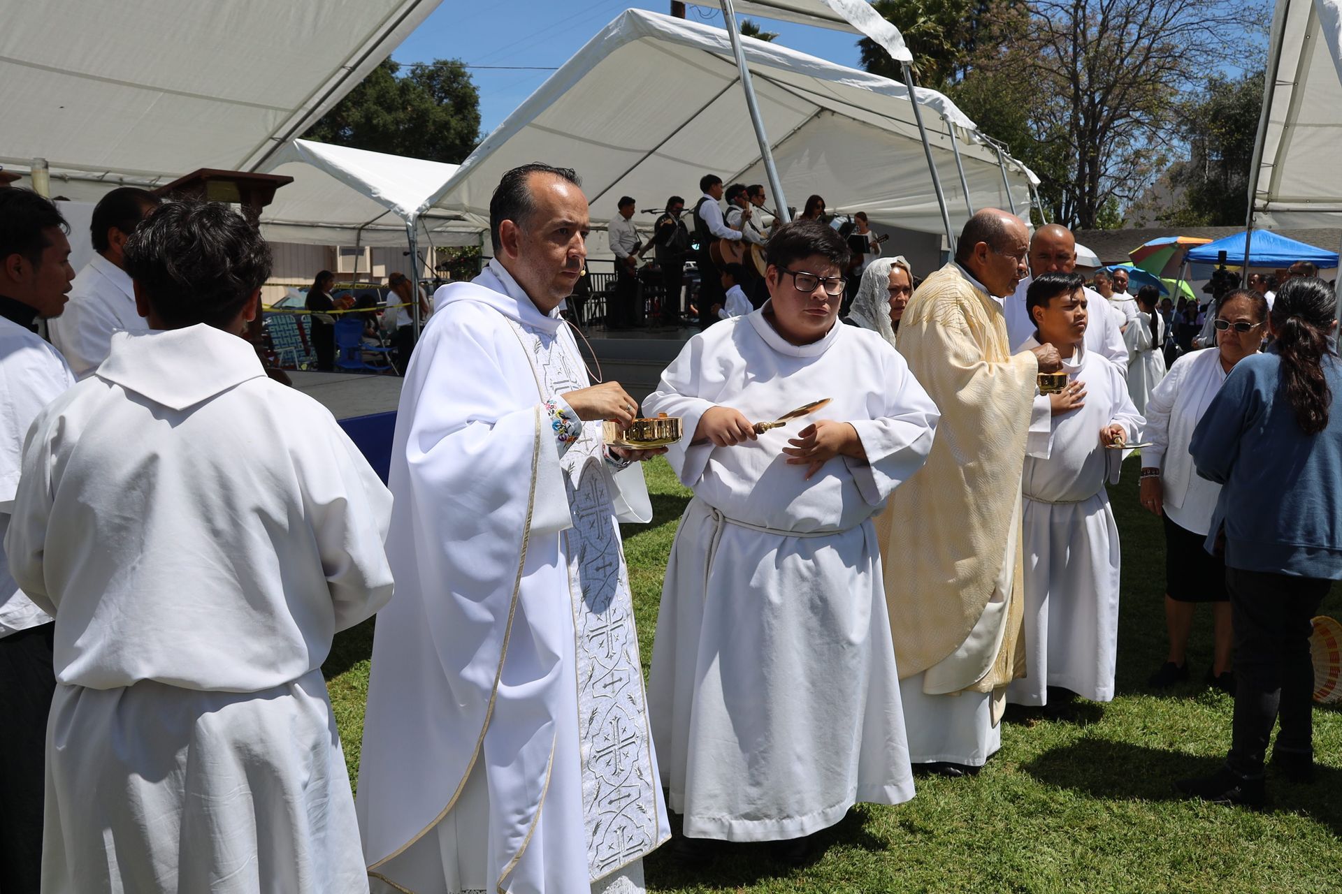 Clergy in white robes stand outdoors during a religious ceremony under a tent.