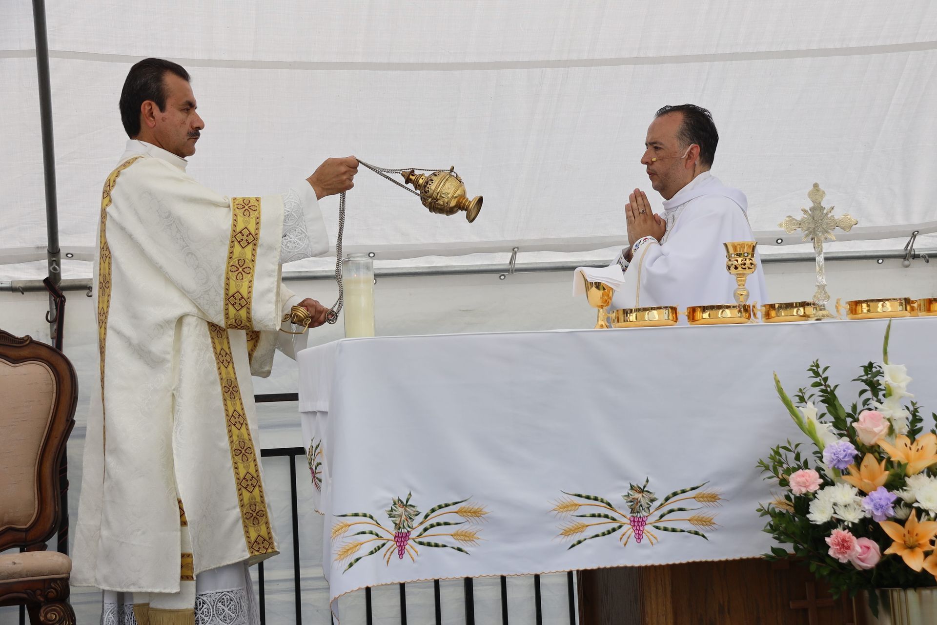 Priest elevates a chalice during Mass at an altar with another priest seated nearby.