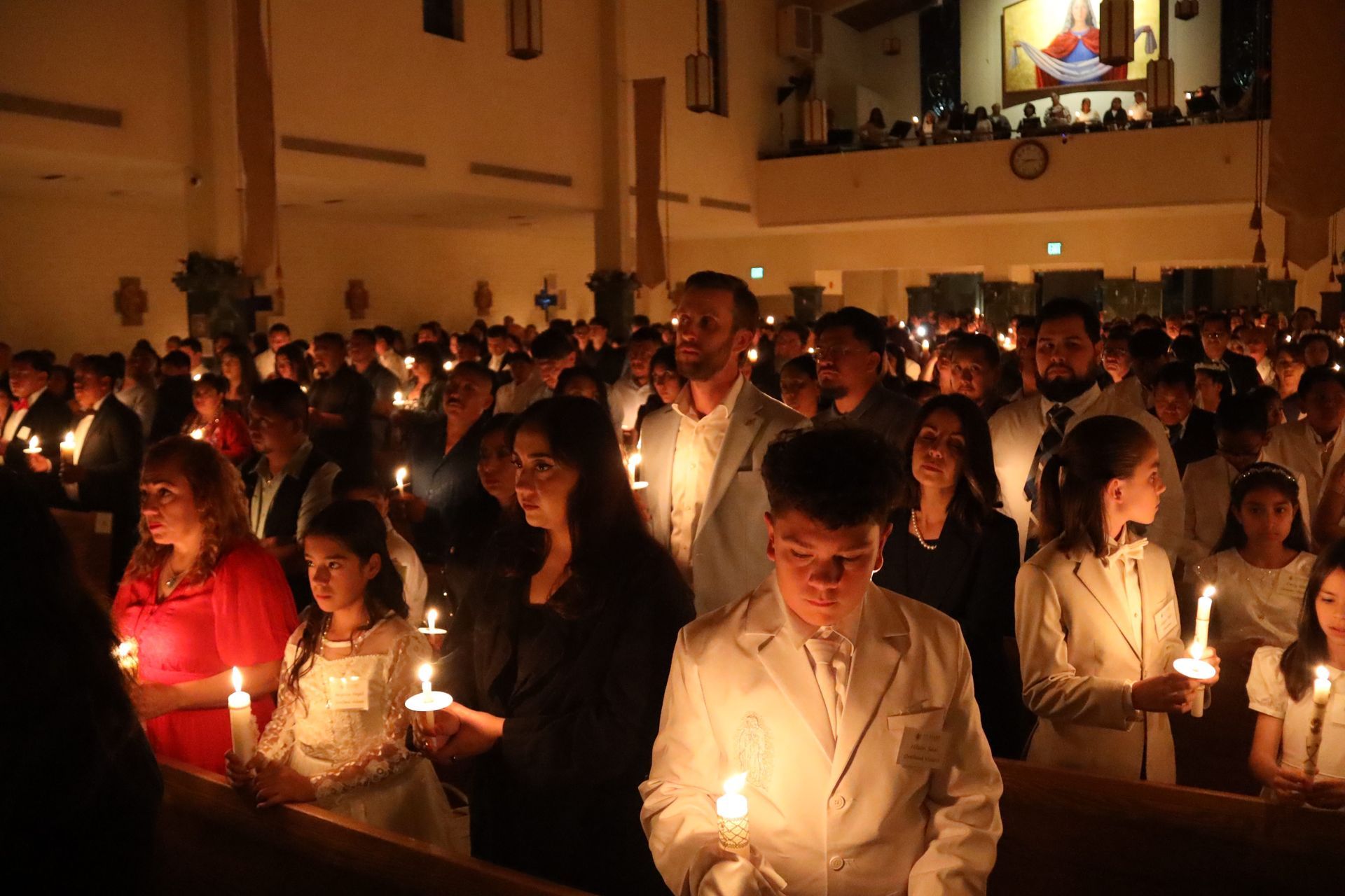 People holding lit candles during a dimly lit indoor vigil or ceremony