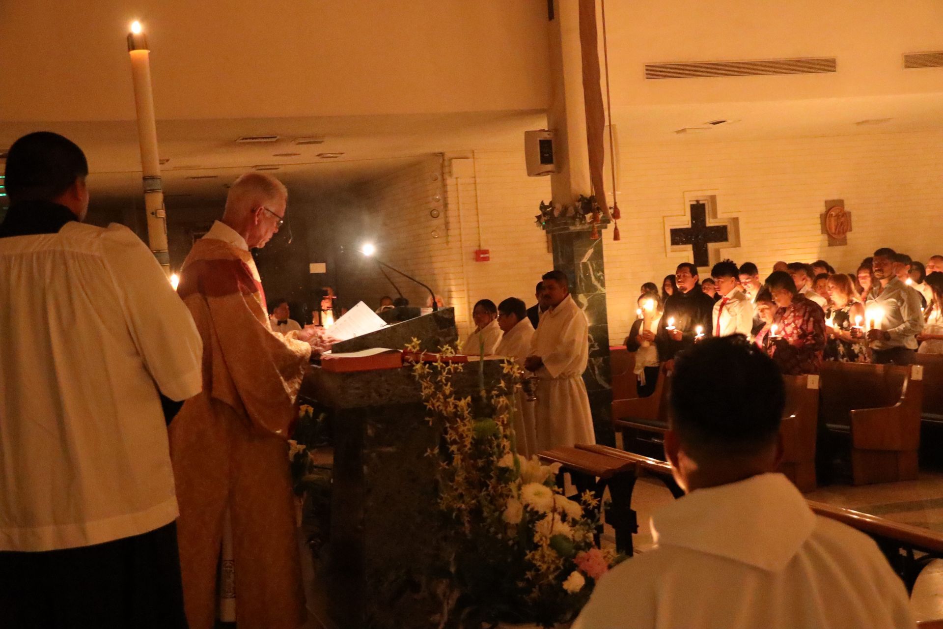 Candlelit church service with a priest reading at the altar and congregants seated in pews