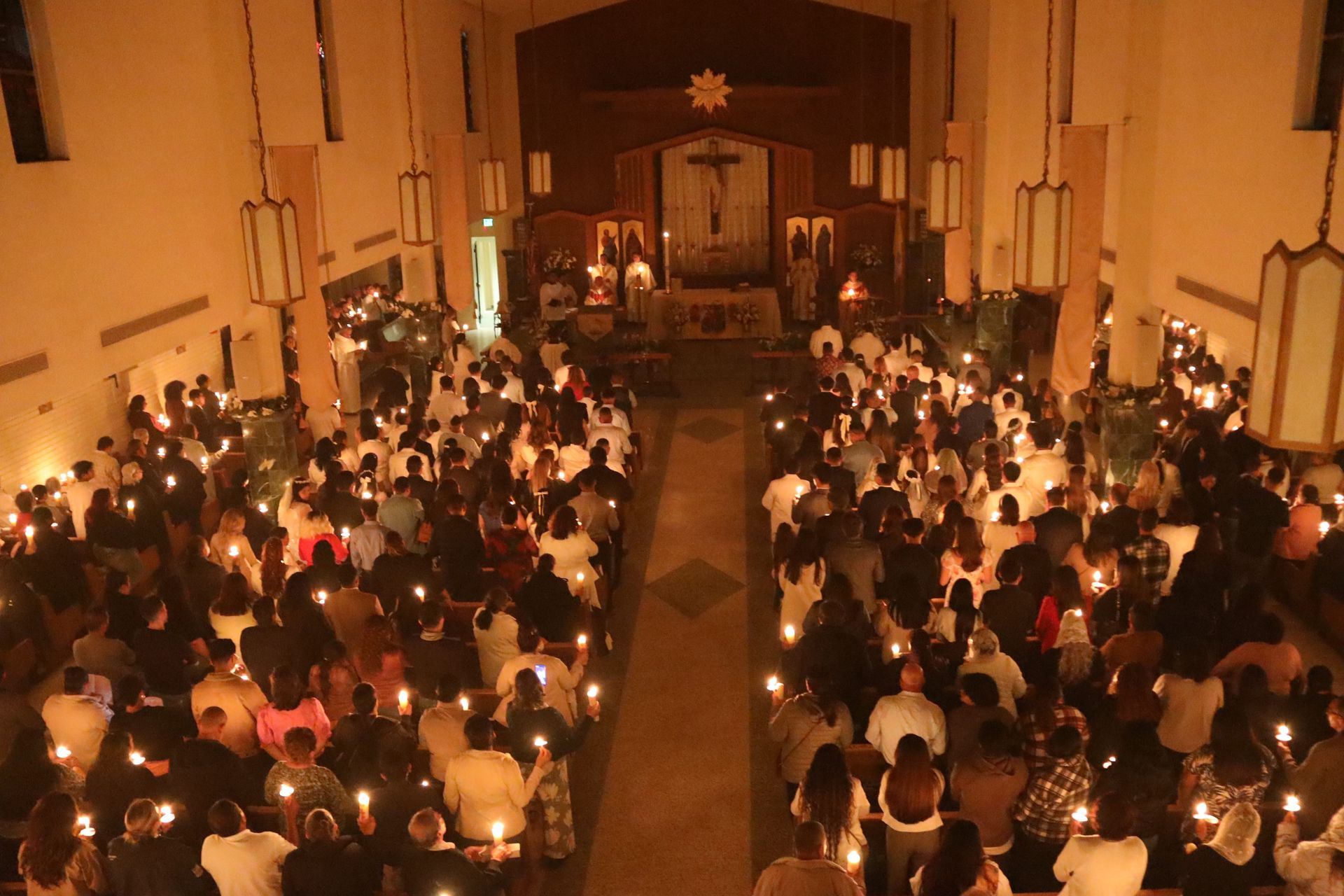 Crowded candlelit church service with people seated in pews facing the altar