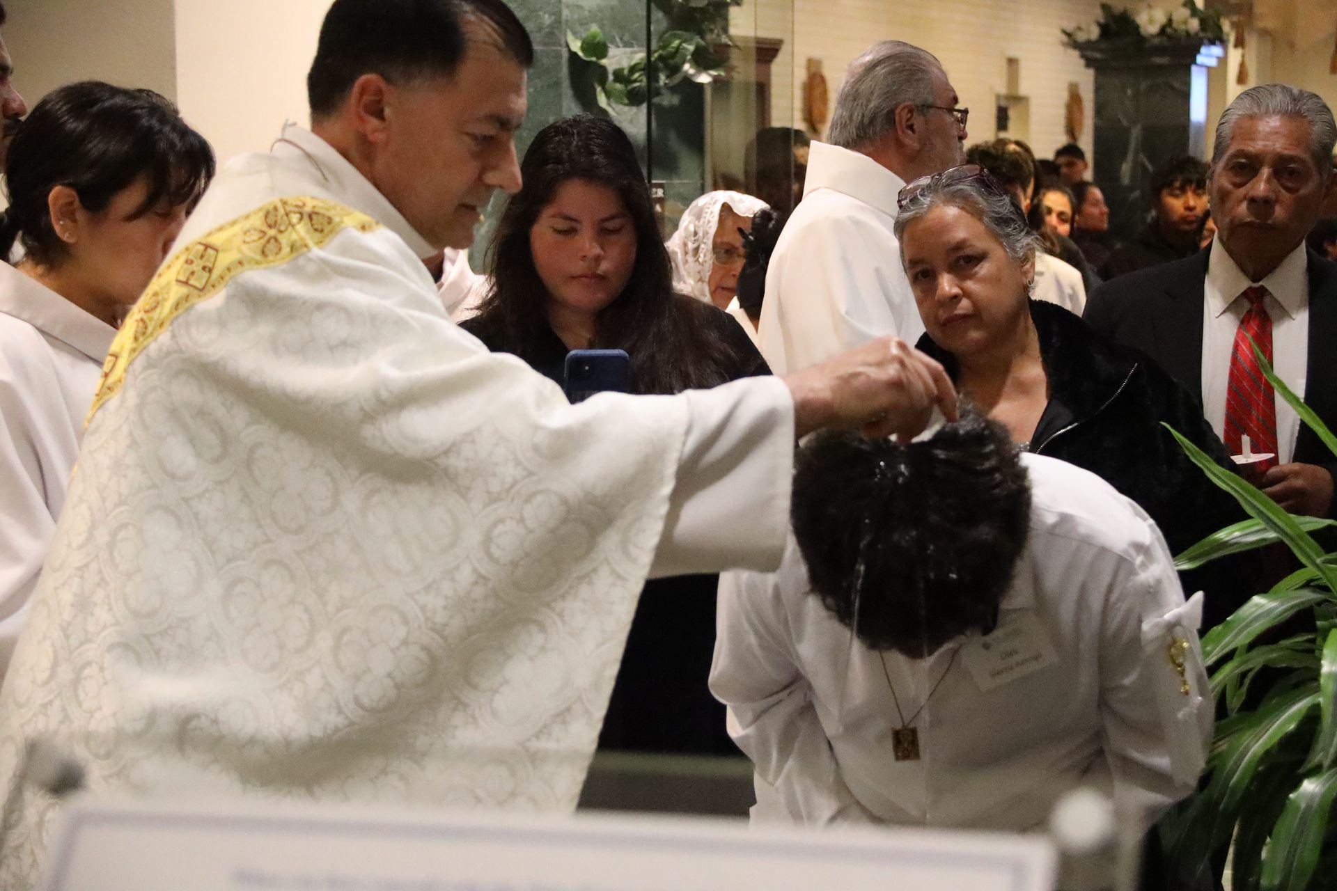 Priest blessing a bowed person during a church ceremony, with onlookers nearby