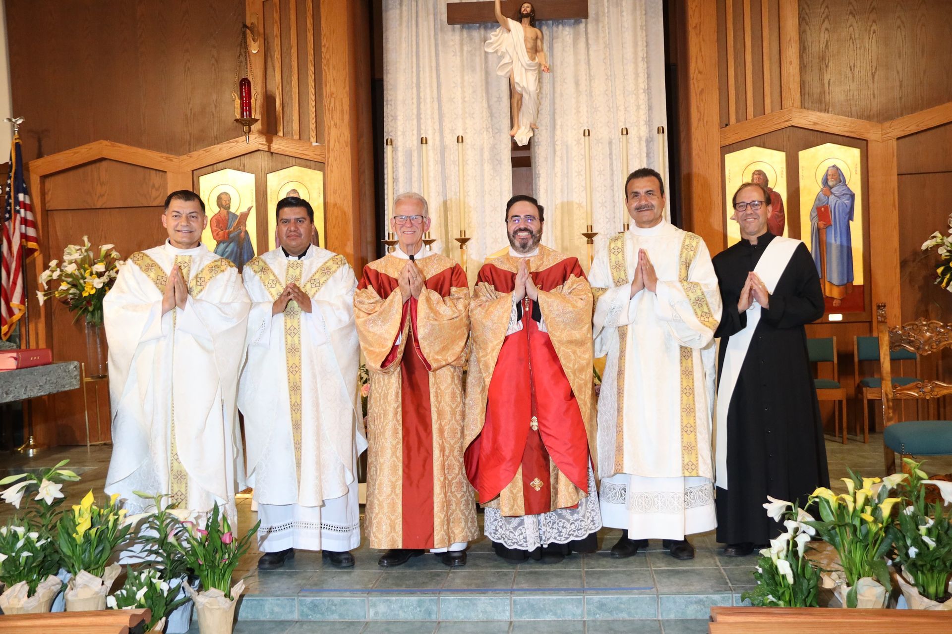 Clergy in white, gold, red, and black vestments stand together on a church altar during a ceremony.