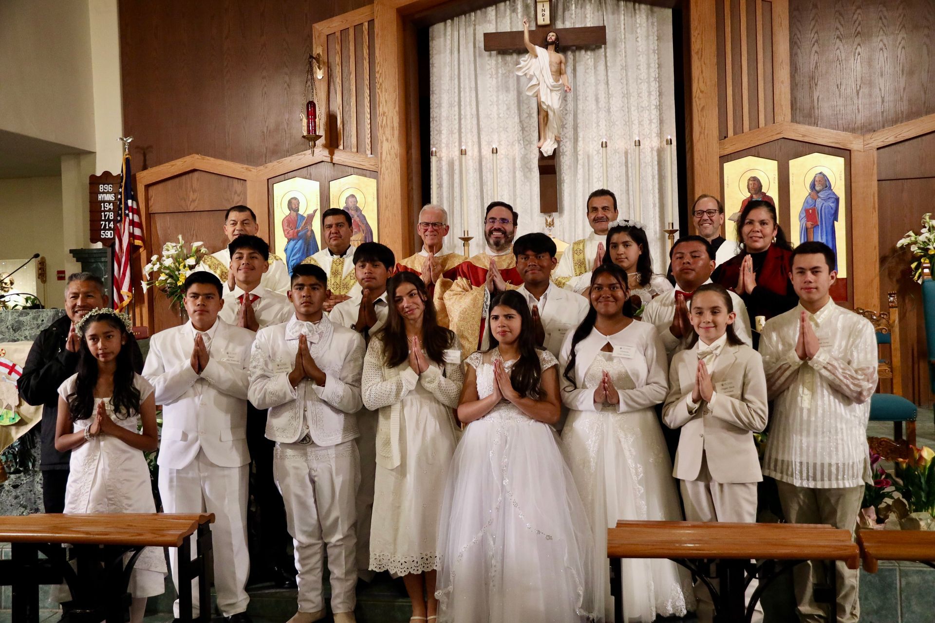 Group of children and adults in white outfits posing inside a church before a crucifix.