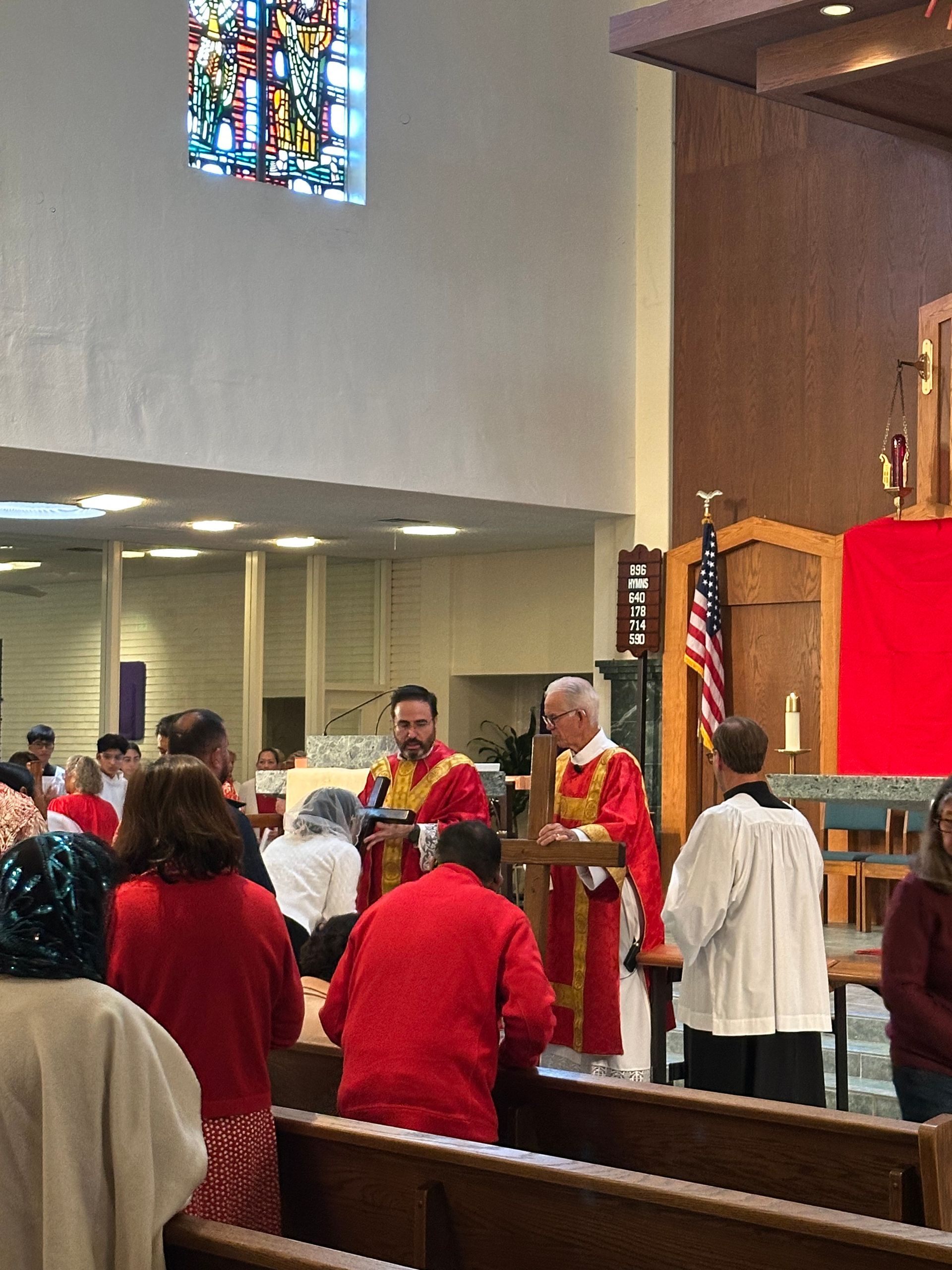 Congregation standing in church pews during a service at the altar with red cloth and candles.