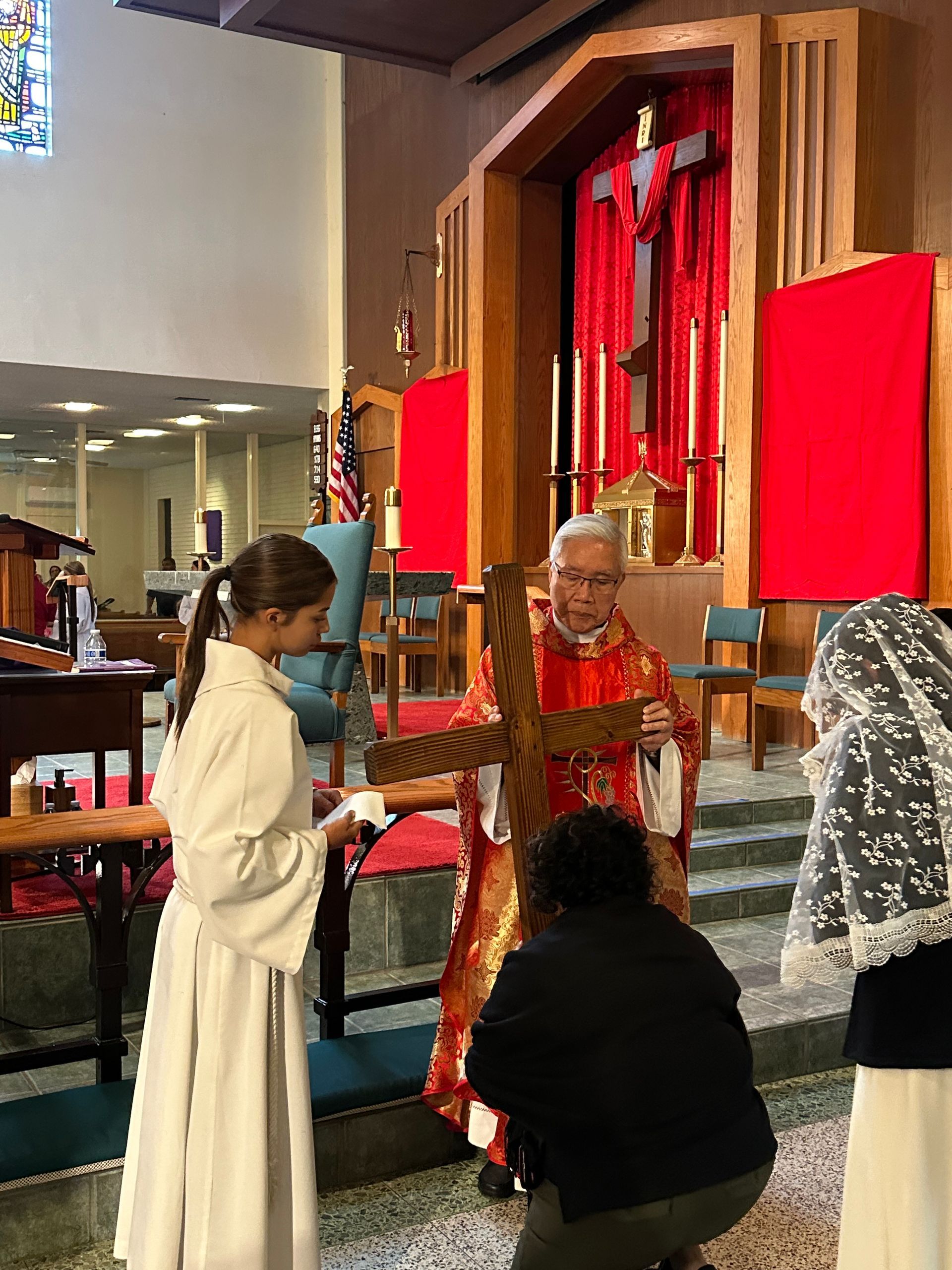 People in a church-like interior holding a red cross near an altar and red drapes