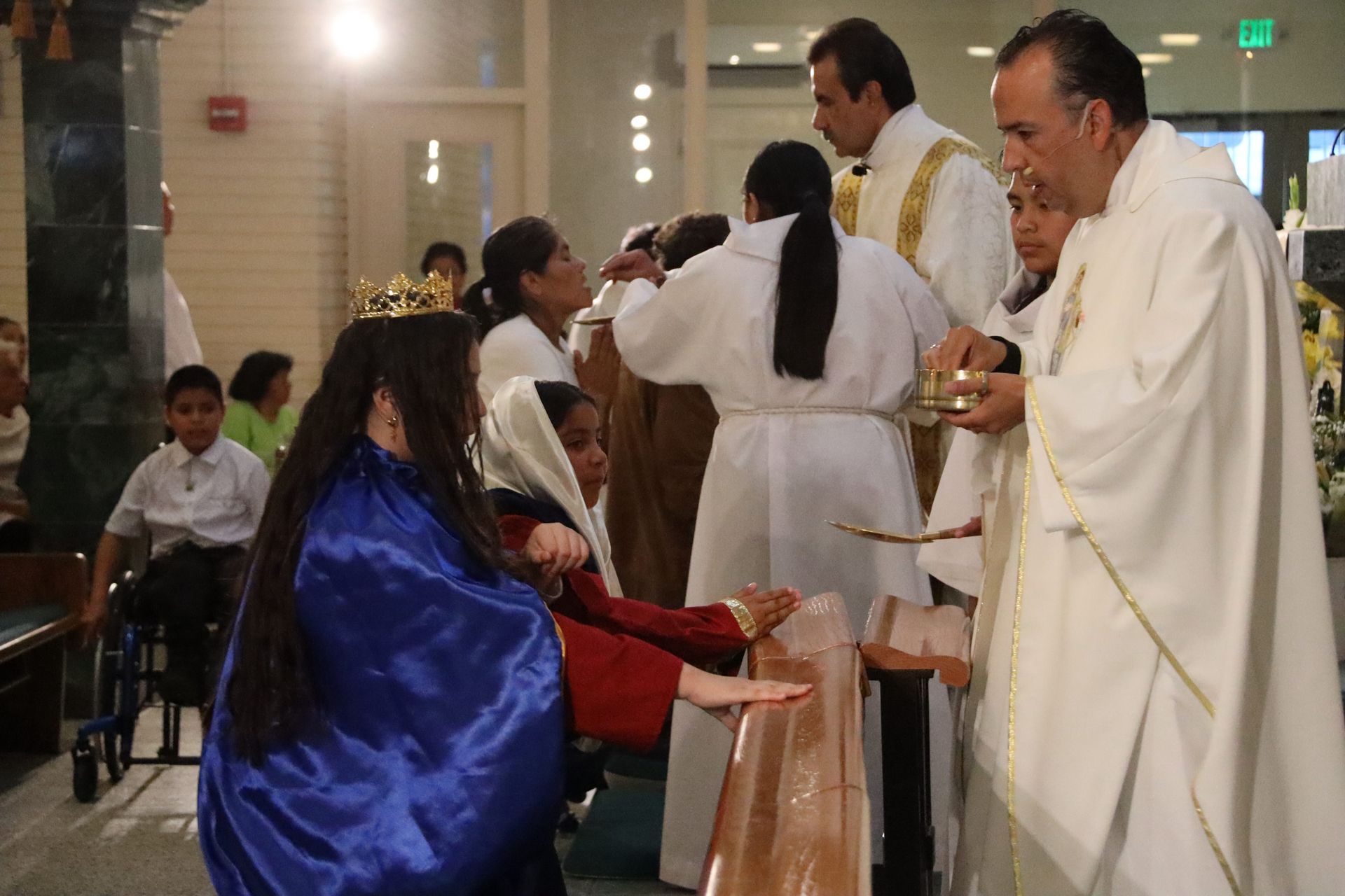 Priest giving communion to a seated woman in a blue shawl during a church service