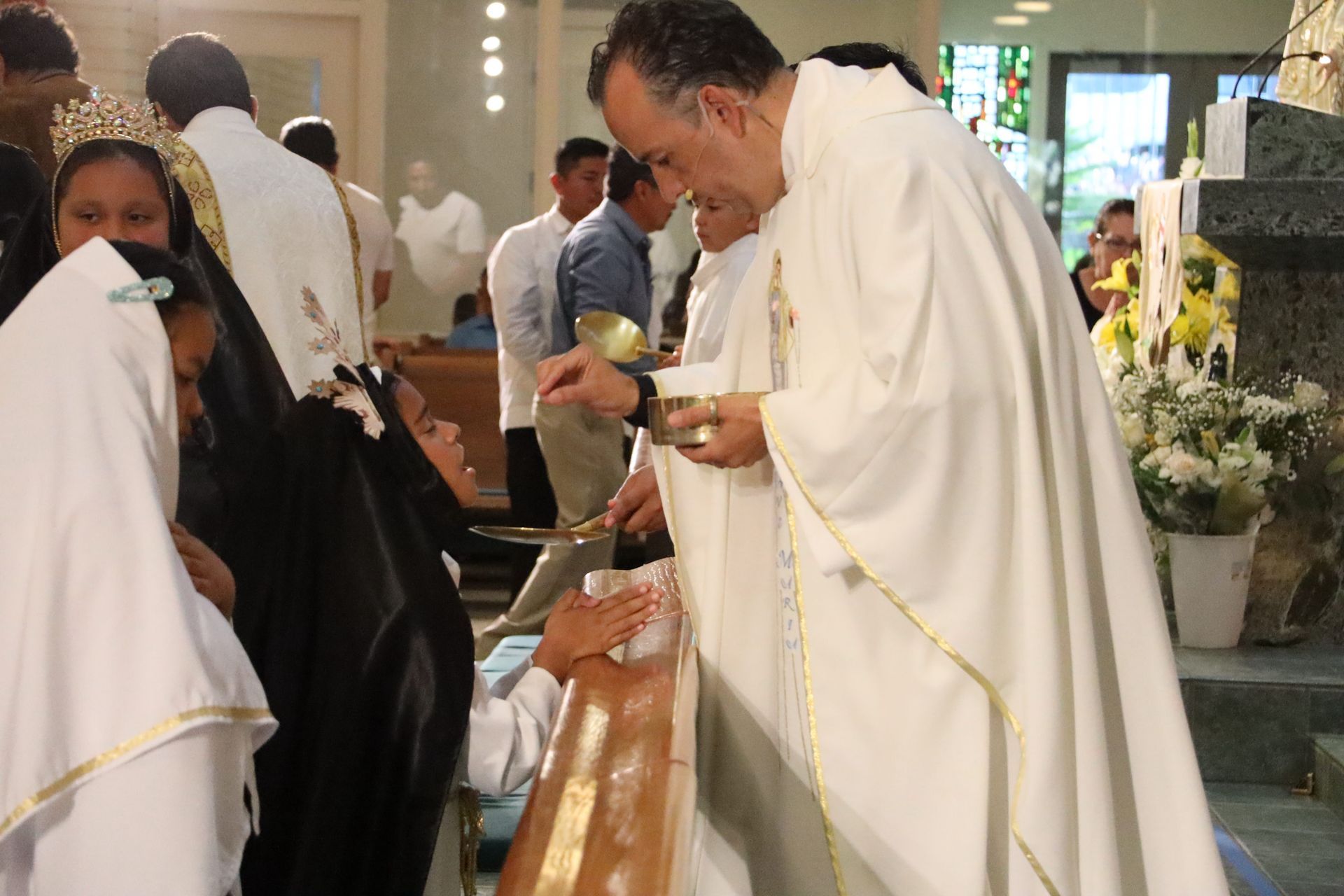 People in white robes at a church ceremony, one man leaning forward to hand out communion.