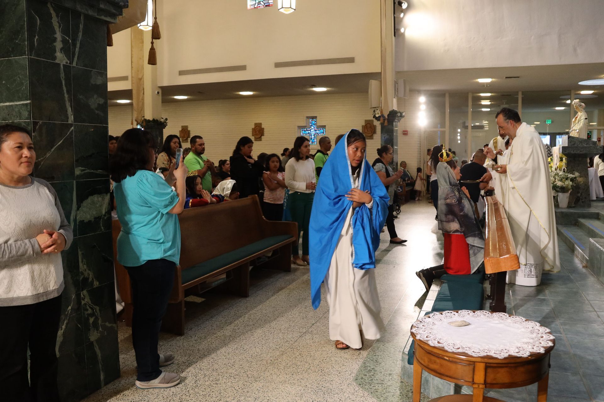 Church procession with clergy in blue and white robes walking through a crowded sanctuary.