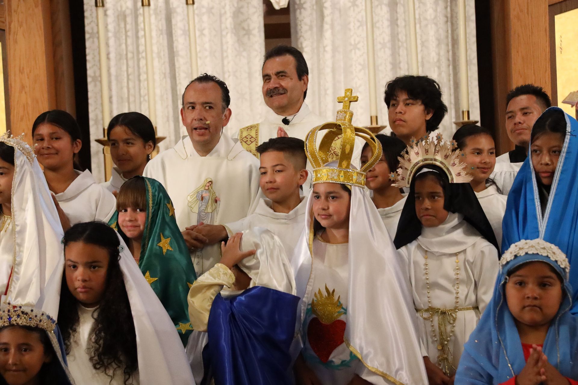 Children and adults in white and colorful robes posing at a church ceremony, one child wearing a gold crown