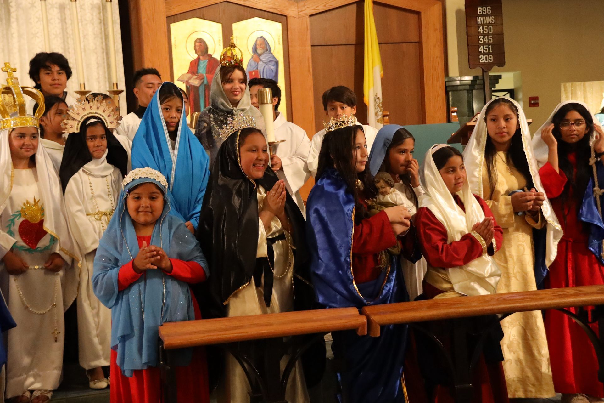 Children in colorful robes standing in a church, some with hands clasped in prayer